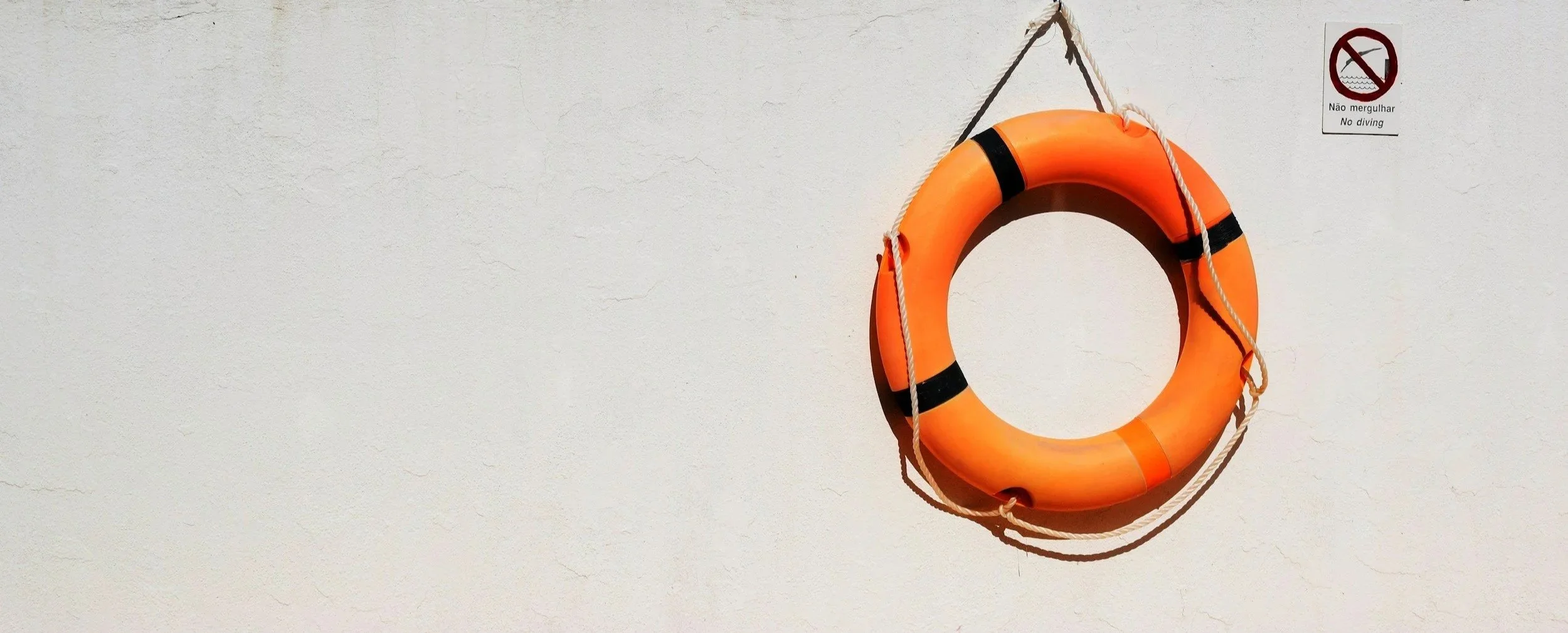 Orange lifebuoy hanging on a white wall with a no diving sign in Portuguese and English.
