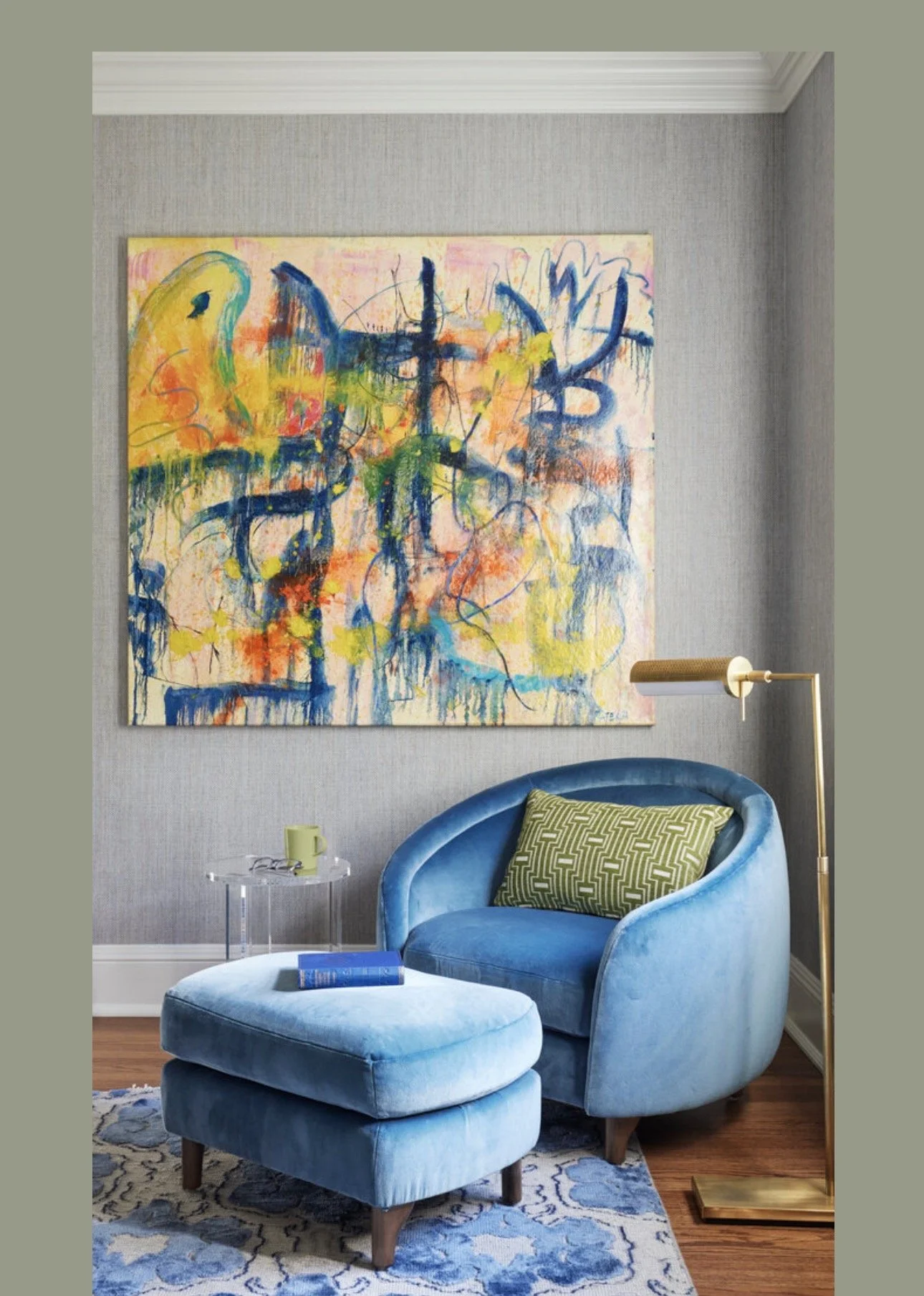Cozy luxury living room corner design in Atlanta with a blue velvet armchair and ottoman, brass floor lamp, and modern side table. Styled with colorful abstract artwork and layered textures, this space creates a warm, inviting, and designer-curated a