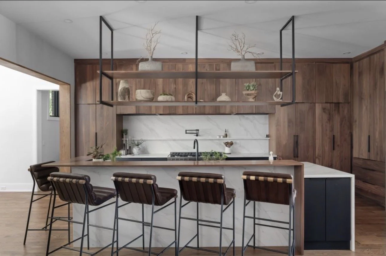 Modern kitchen design in Atlanta with a white marble island, wood cabinetry, and leather bar stools. Open shelving with curated decor and greenery adds warmth, blending contemporary interior design with a sophisticated, organic aesthetic.