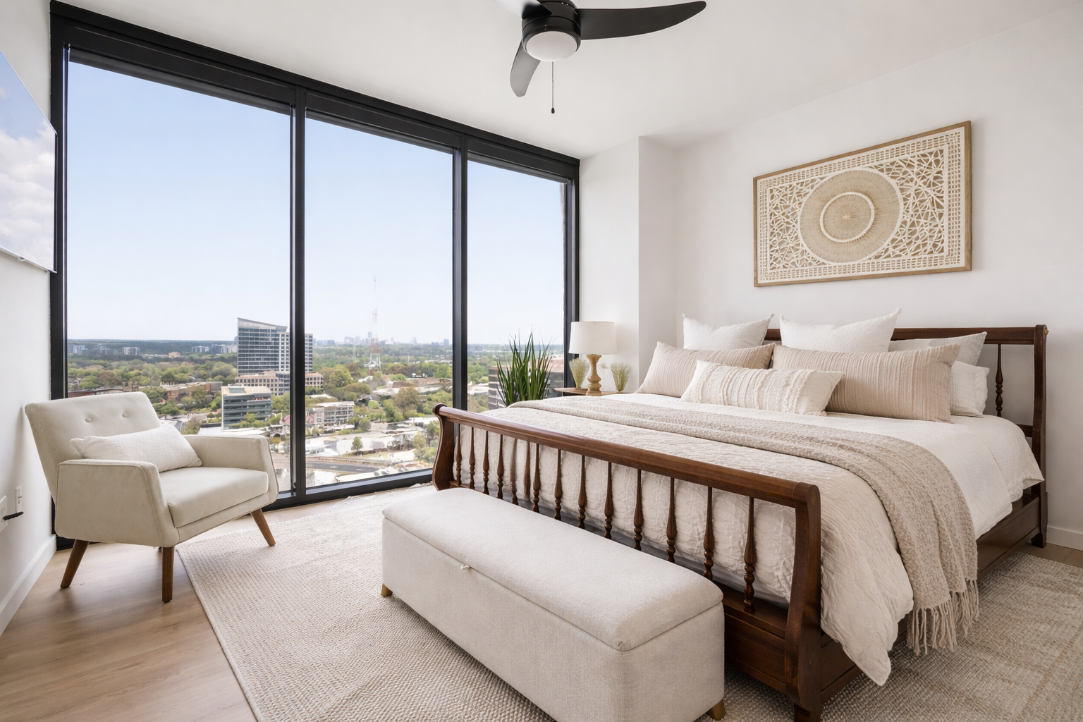 Luxury bedroom design in Atlanta featuring floor-to-ceiling windows with city skyline views, a wood bed with layered neutral bedding, and a bench at the foot of the bed. Styled with natural light, soft textures, and curated decor, this space reflects