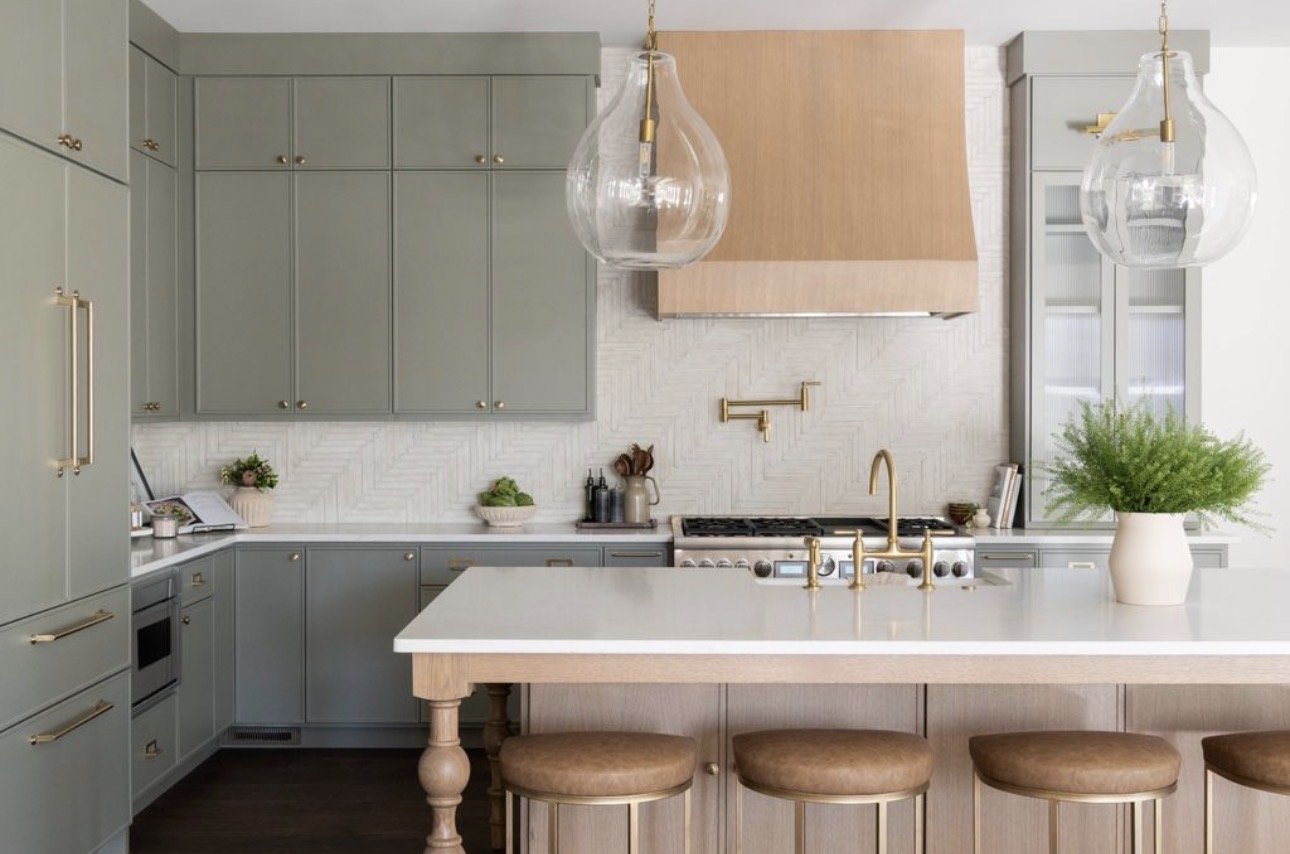 Contemporary kitchen design in Atlanta with gray cabinetry, a white island, and gold fixtures. Styled with greenery and statement pendant lighting, this space reflects luxury interior design with a modern, elevated finish.