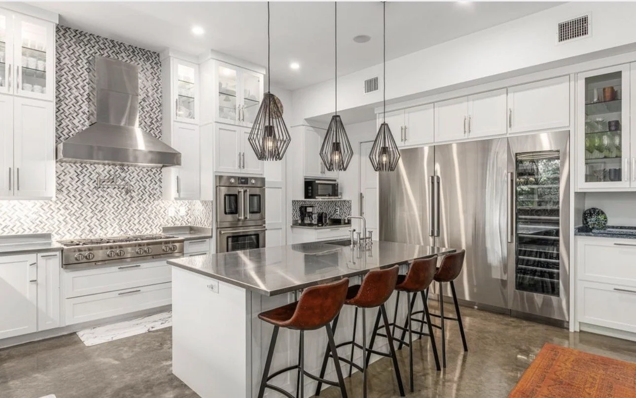 Contemporary kitchen design featuring white cabinetry, stainless steel appliances, and a spacious island with bar seating. Styled with pendant lighting and a geometric backsplash, this Atlanta kitchen balances functionality with elevated modern desig
