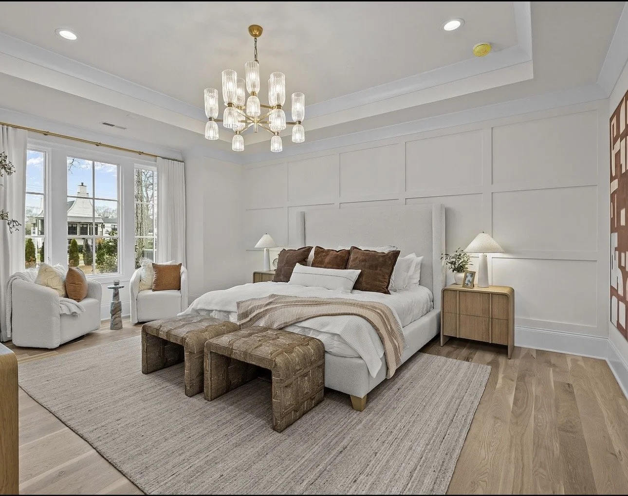 Luxury bedroom design in Atlanta featuring white walls, layered neutral bedding, and a statement chandelier. Styled with wood nightstands, accent chairs, and natural light, this space reflects modern interior design with a calm, elegant, and upscale 