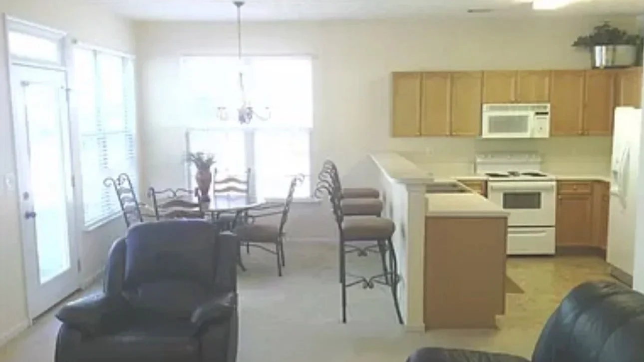 IOriginal open-concept living room and kitchen with dated finishes, wood cabinetry, and basic layout. This space represents the starting point of a home transformation and interior design strategy project in Atlanta.