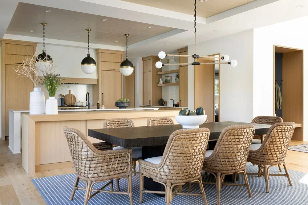 Open-concept kitchen and dining room design in Atlanta featuring light wood cabinetry, a dark dining table, and woven accent chairs. Styled with modern pendant lighting and curated decor, this space blends contemporary interior design with a warm, or