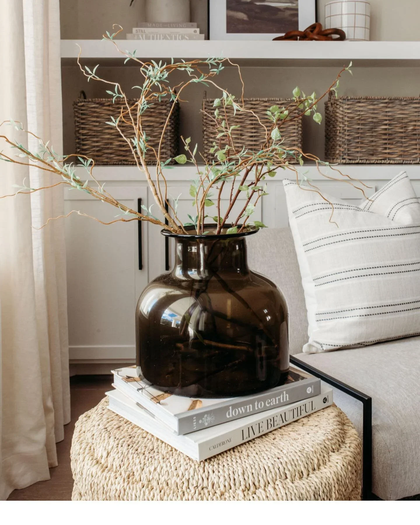 Interior styling detail in an Atlanta living room featuring a glass vase with natural greenery, styled books, and a woven ottoman. This curated vignette highlights luxury home decor, layered textures, and modern interior styling techniques.