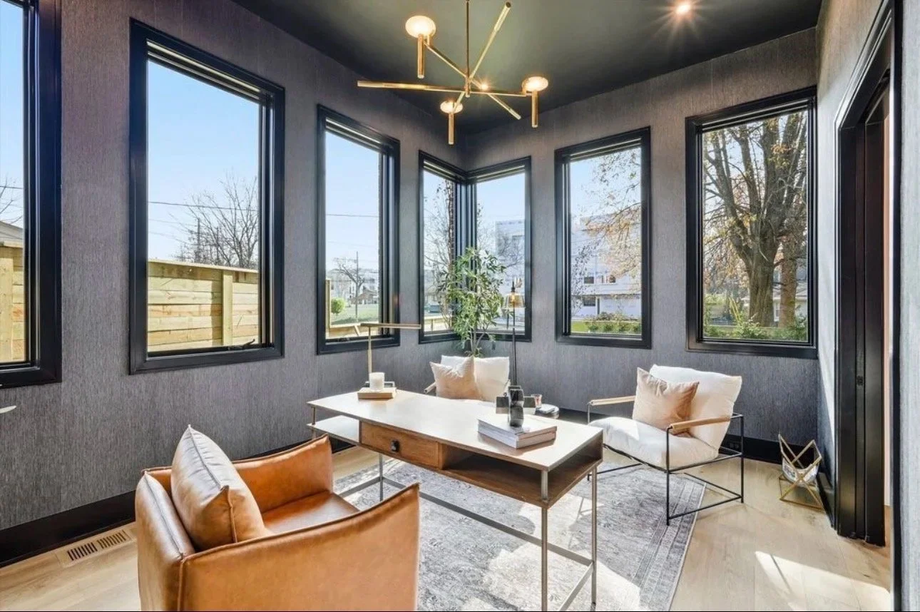 Modern sunroom design with floor-to-ceiling black-framed windows, a tan leather accent chair, and curated neutral seating. This light-filled Atlanta space blends indoor comfort with outdoor views, finished with a statement chandelier and organic deco