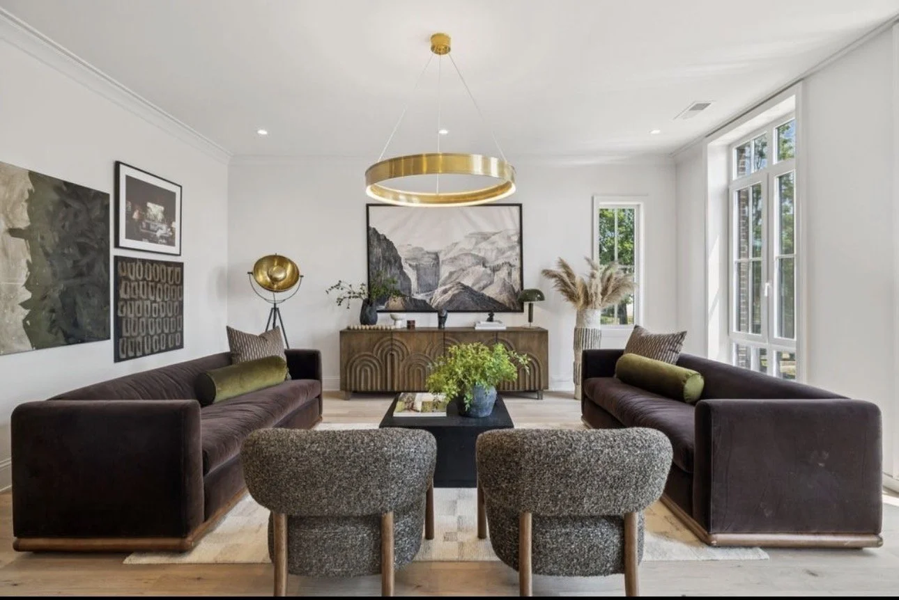 Contemporary living room interior design in Atlanta featuring dual brown velvet sofas, gray accent chairs, and a modern black coffee table. Large windows provide natural light, while curated decor and greenery enhance this upscale, balanced living sp