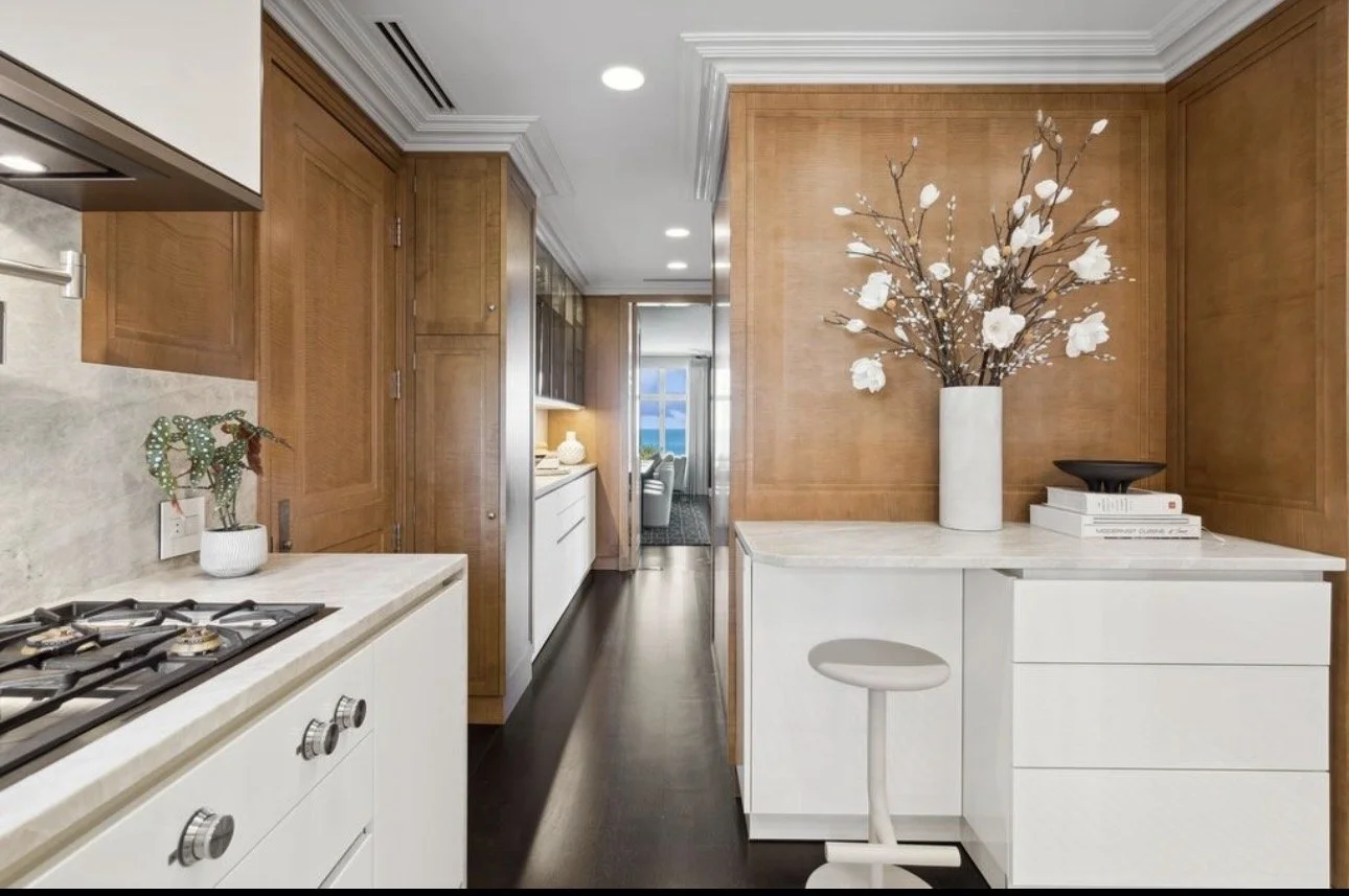 Modern kitchen design in Atlanta featuring white cabinets, marble countertops, and warm wood paneling. Styled with curated decor and natural textures, this space blends contemporary interior design with a sophisticated, organic aesthetic.