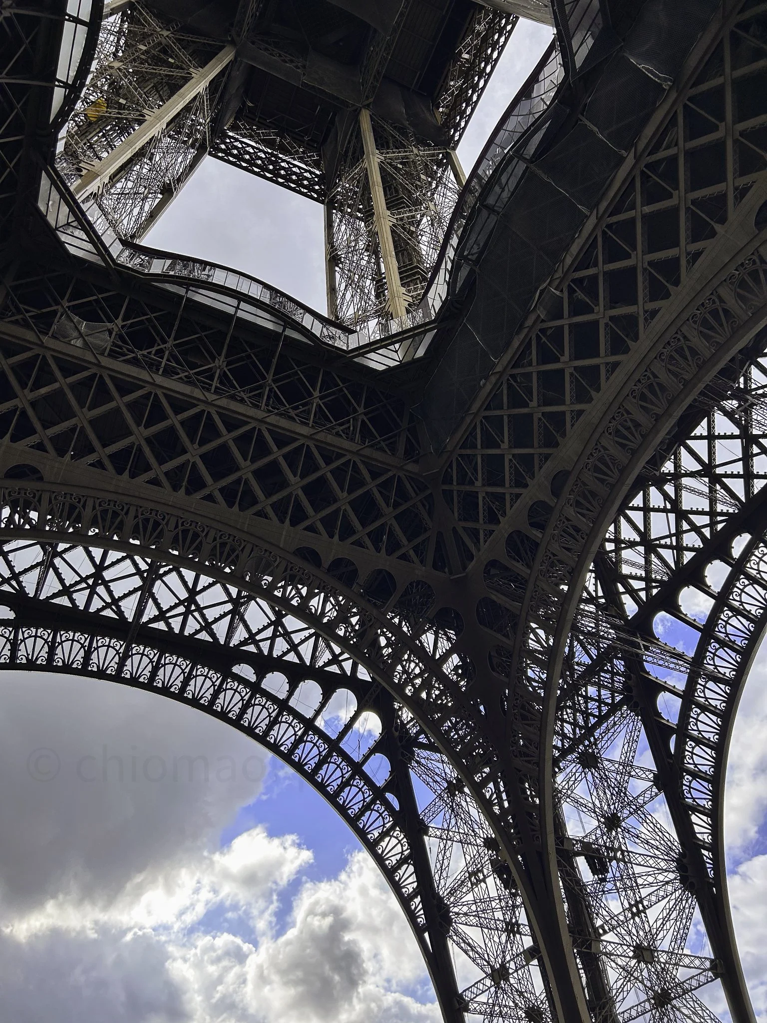 Underneath the Eiffel Tower looking up at the intricate iron lattice structure and the sky beyond.