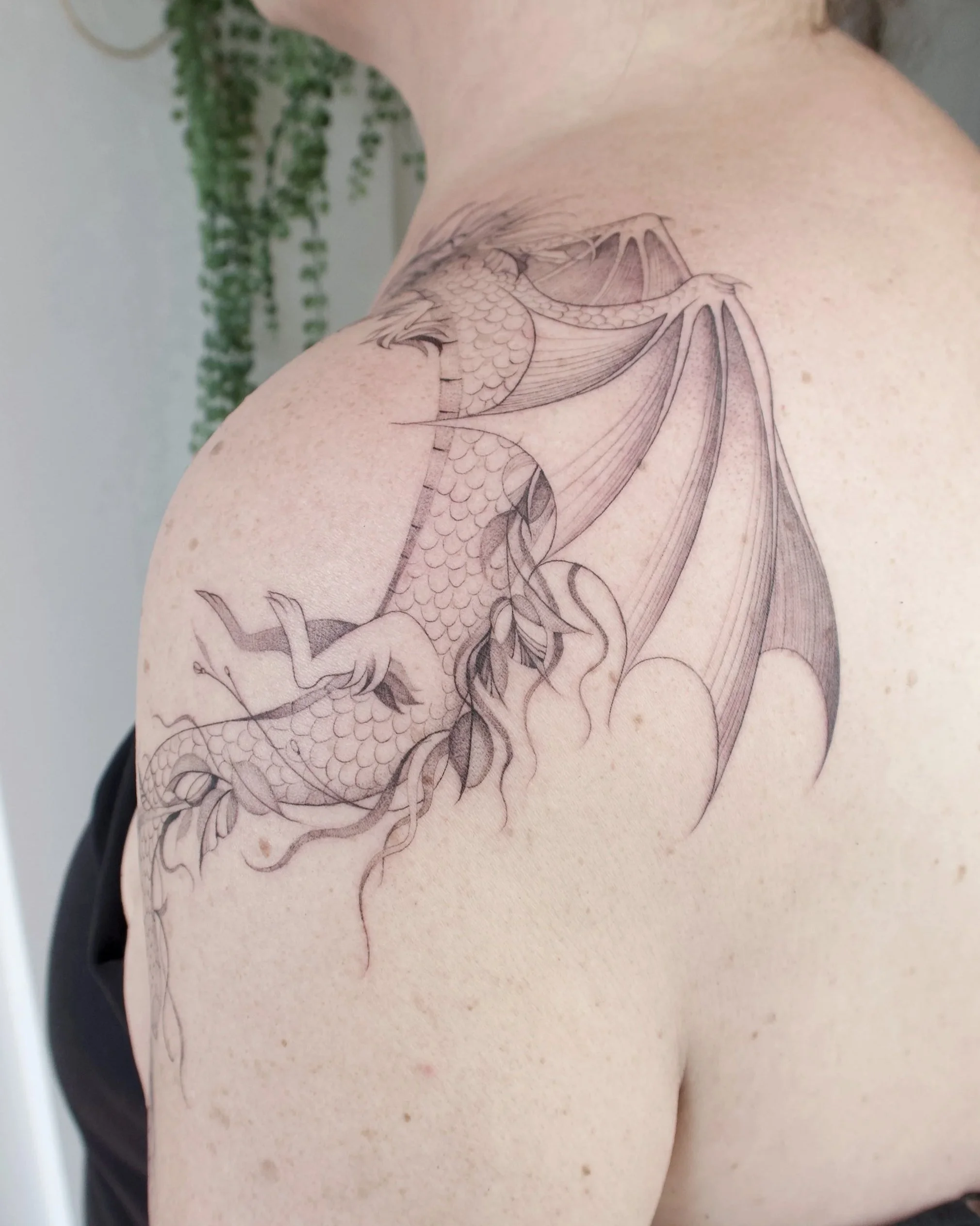 fineline draken tattoo rondom schouder vrouw