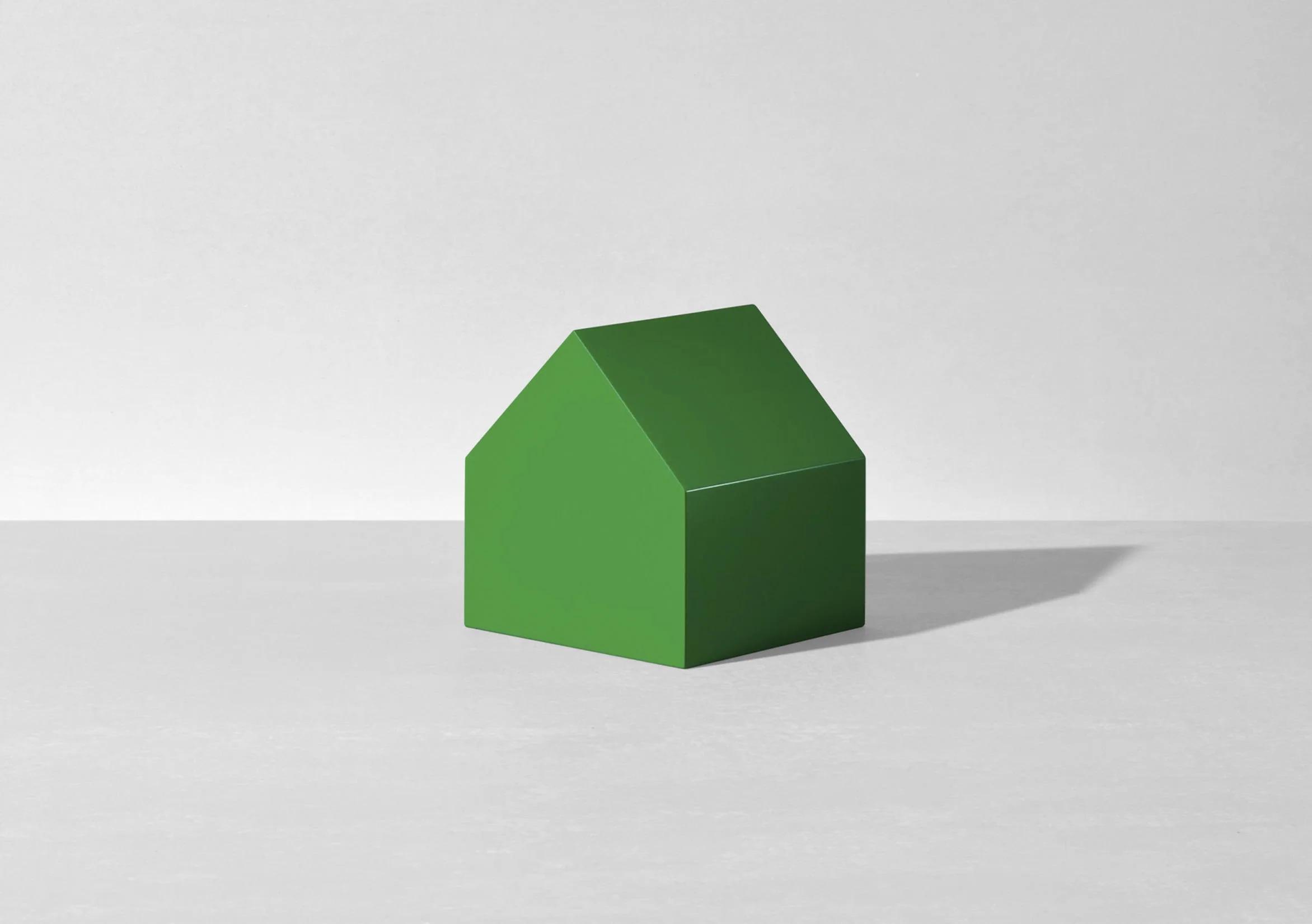 Green house-shaped object on a light gray surface against a light gray wall.