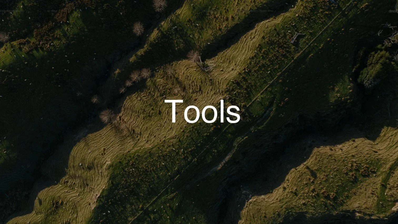Aerial view of a mountainous landscape with a forested area on the upper part and open grassy slopes; the word 'Tools' is centered on the image.