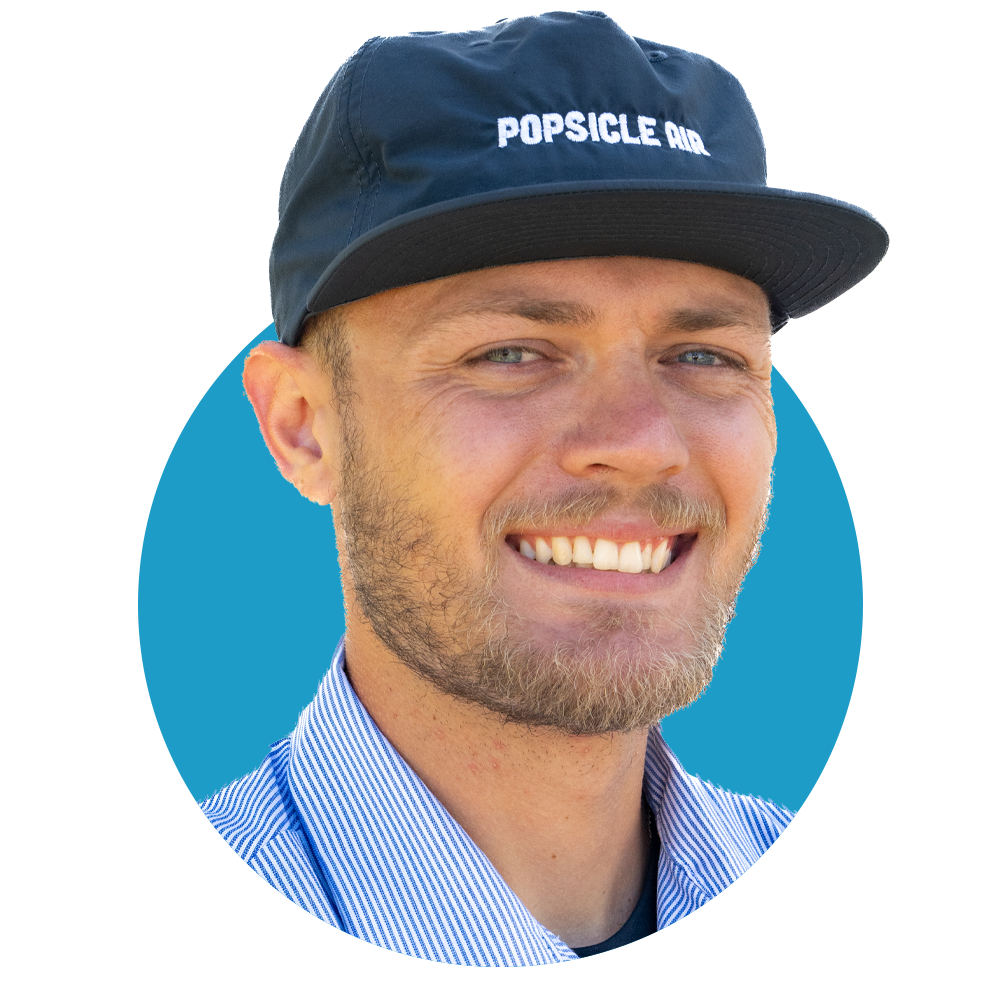 A smiling man wearing a black cap with 'POPSICLE AIR' written on it, a blue and white striped shirt, and a beard, with a digital background.