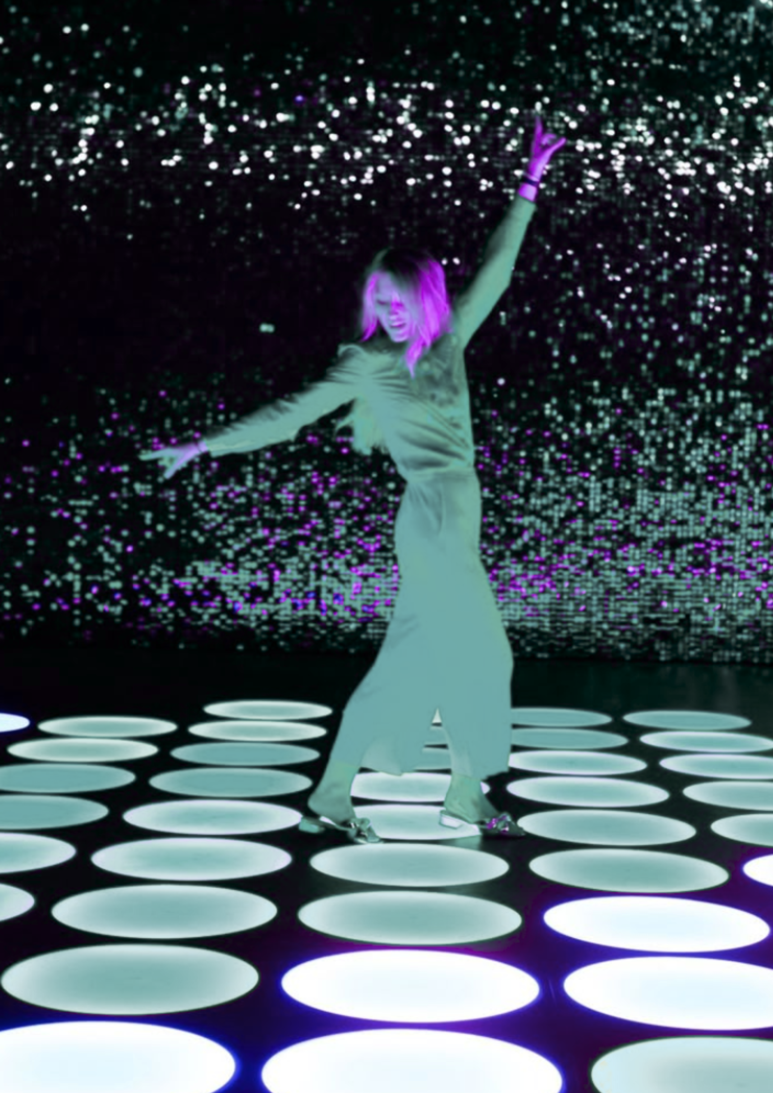 A woman with pink hair dancing on an illuminated floor with large circular lights in a dark space, with a background of multicolored, sparkling lights.