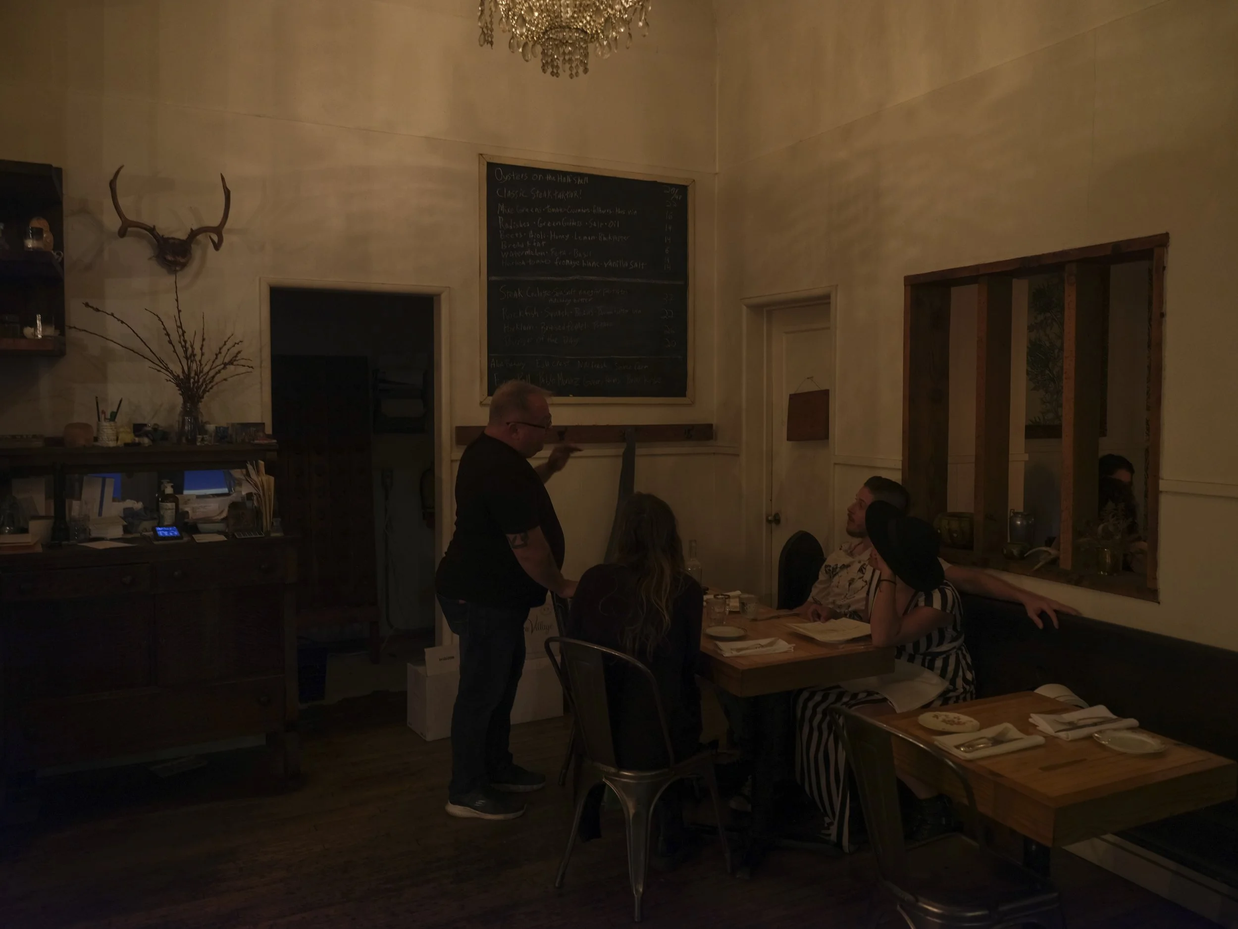 Owner Patrick presents the menu in a dimly lit dining room at Thistle Restaurant. Western decor is visible.
