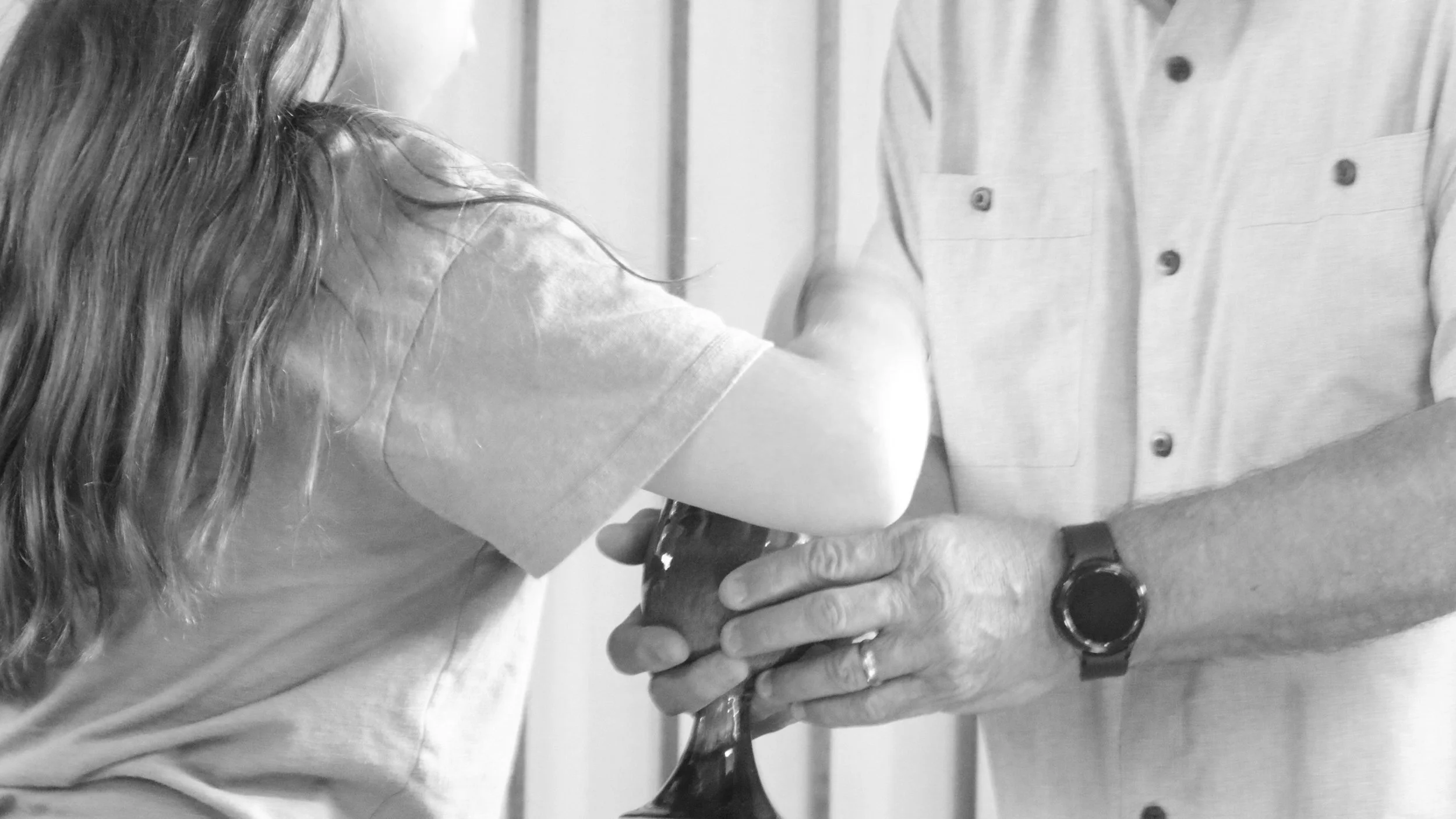 Person pouring a drink into a glass held by another person, in black and white.