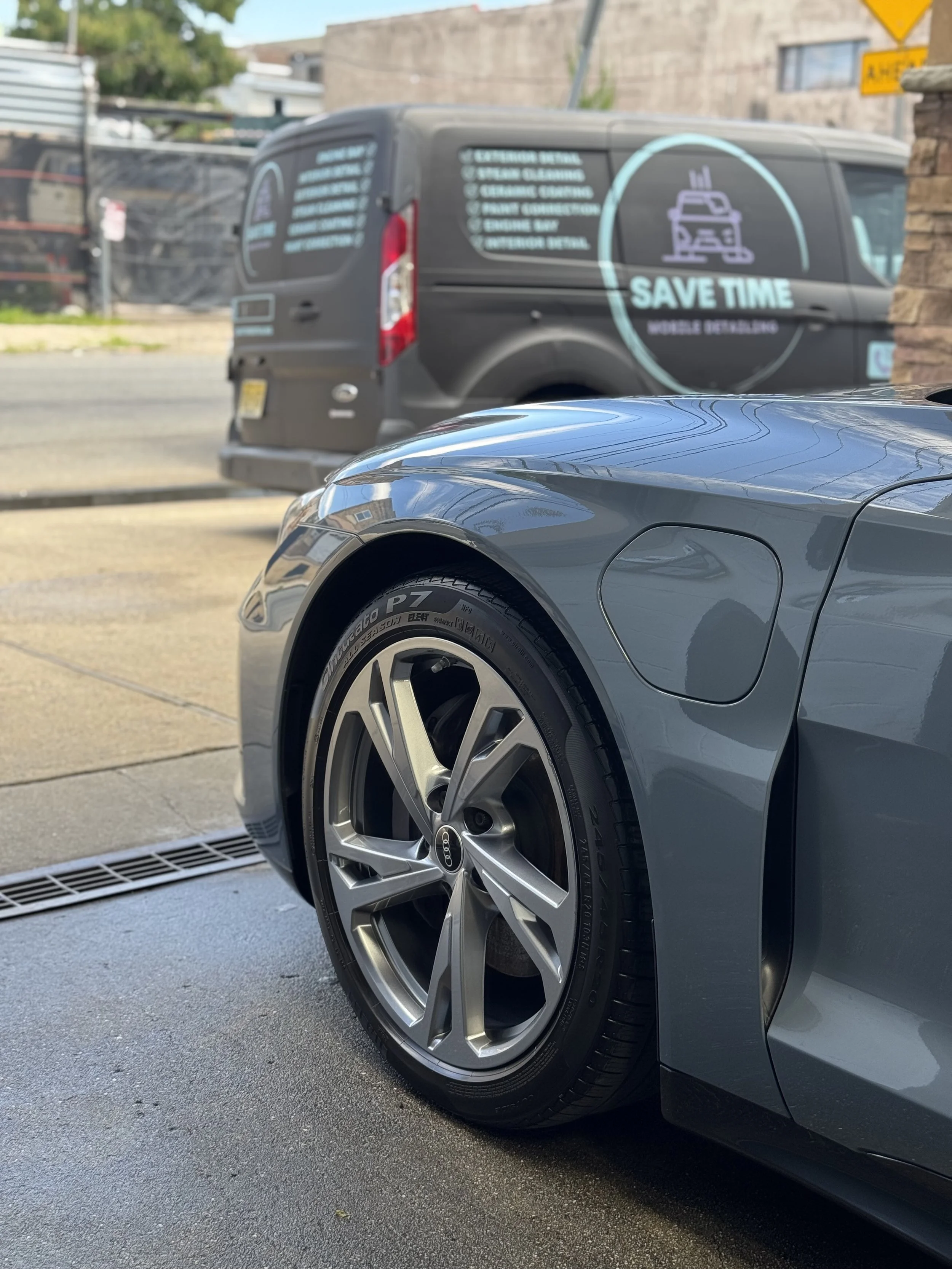 Close-up of the front part of a gray sports car, showing the wheel and tire, parked on the street.