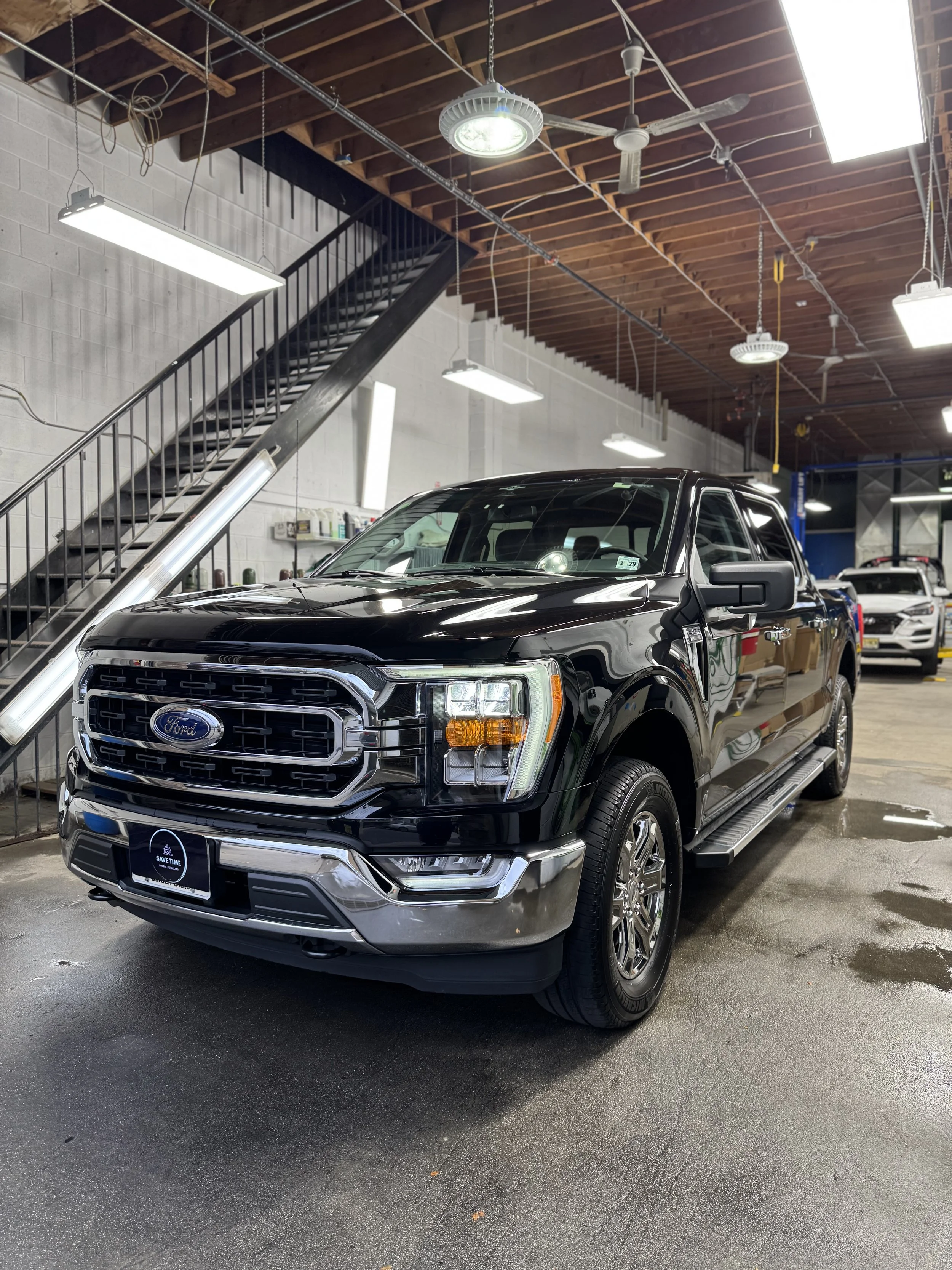 Black Ford pickup truck inside a showroom with a concrete floor, industrial ceiling, and staircase in the background.
