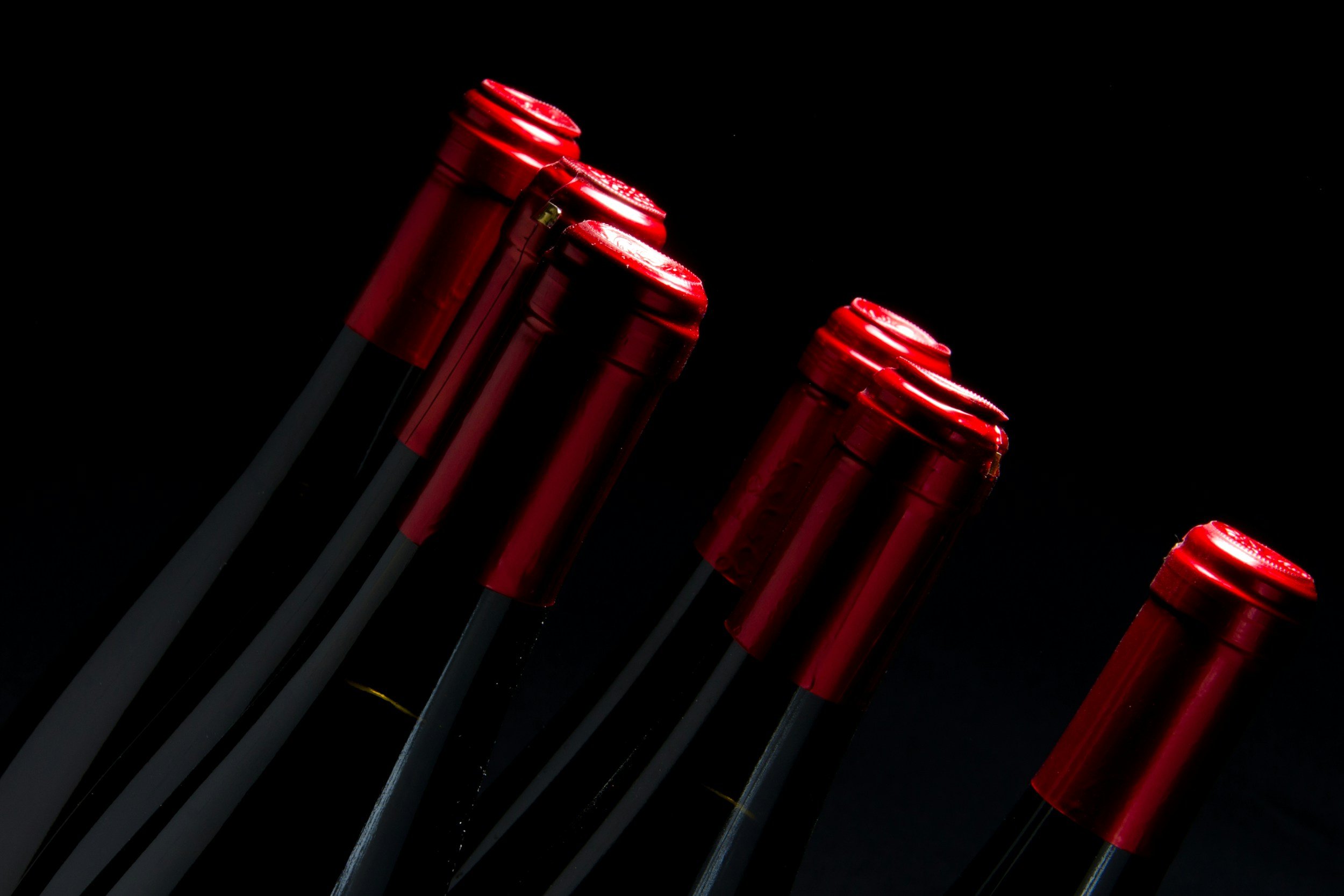 Red wine bottle tops with capsules against a black background.