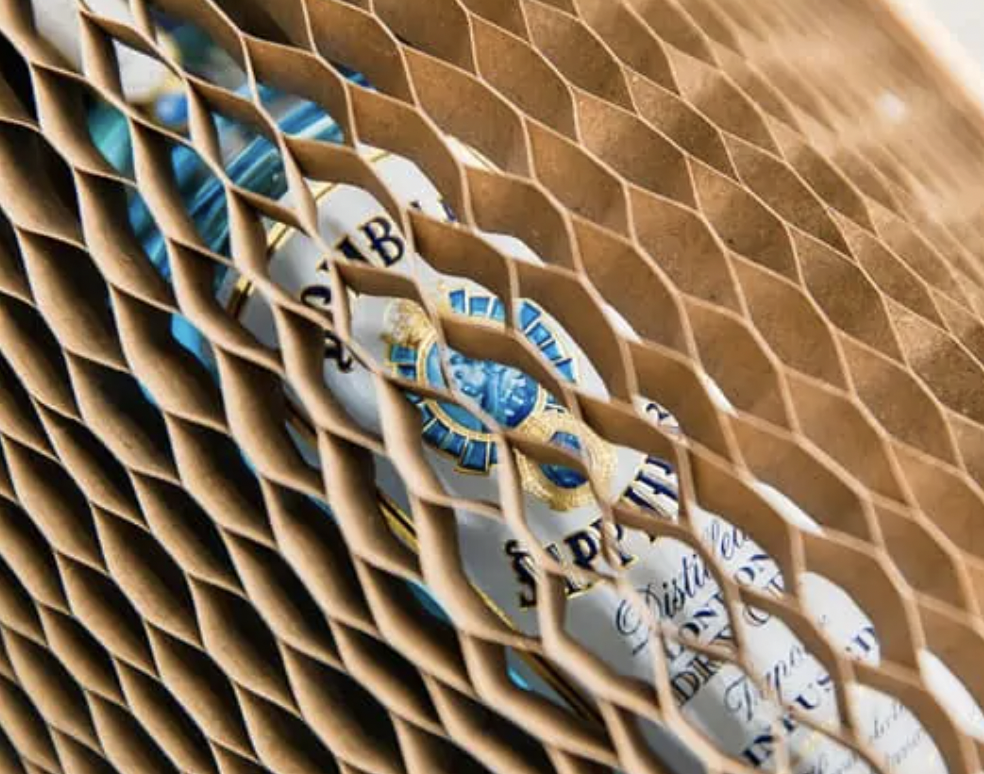 A bottle of Bombay Sapphire gin partially visible through a honeycomb-patterned cardboard packaging.