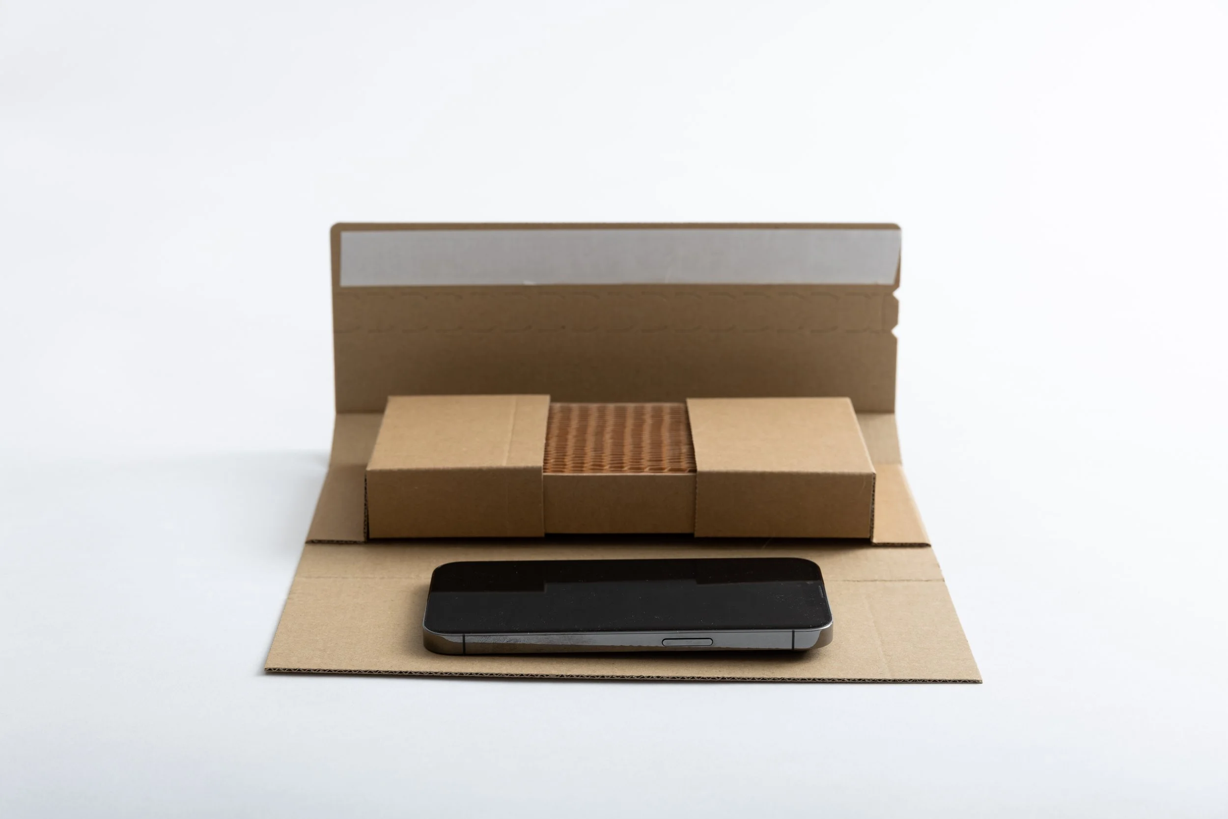 A black smartphone resting on a flat cardboard surface in front of a white and brown cardboard box.