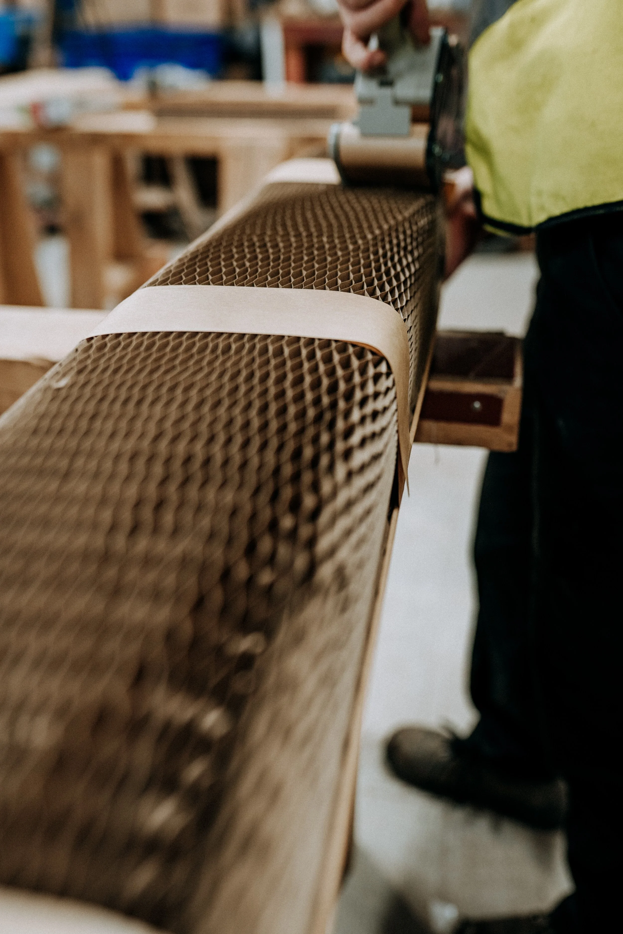 Person using a tool on a roll of honeycomb cardboard packaging in a workshop setting.