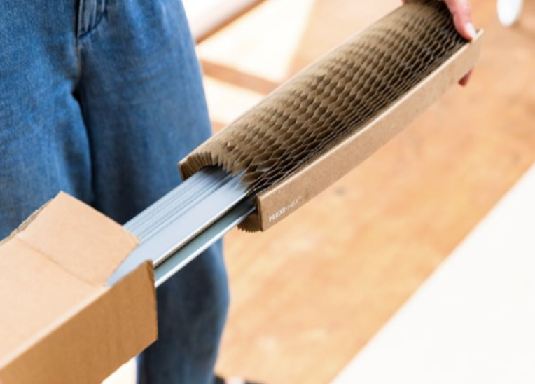Person holding a cardboard packaging with honeycomb padding and metal strips inside.
