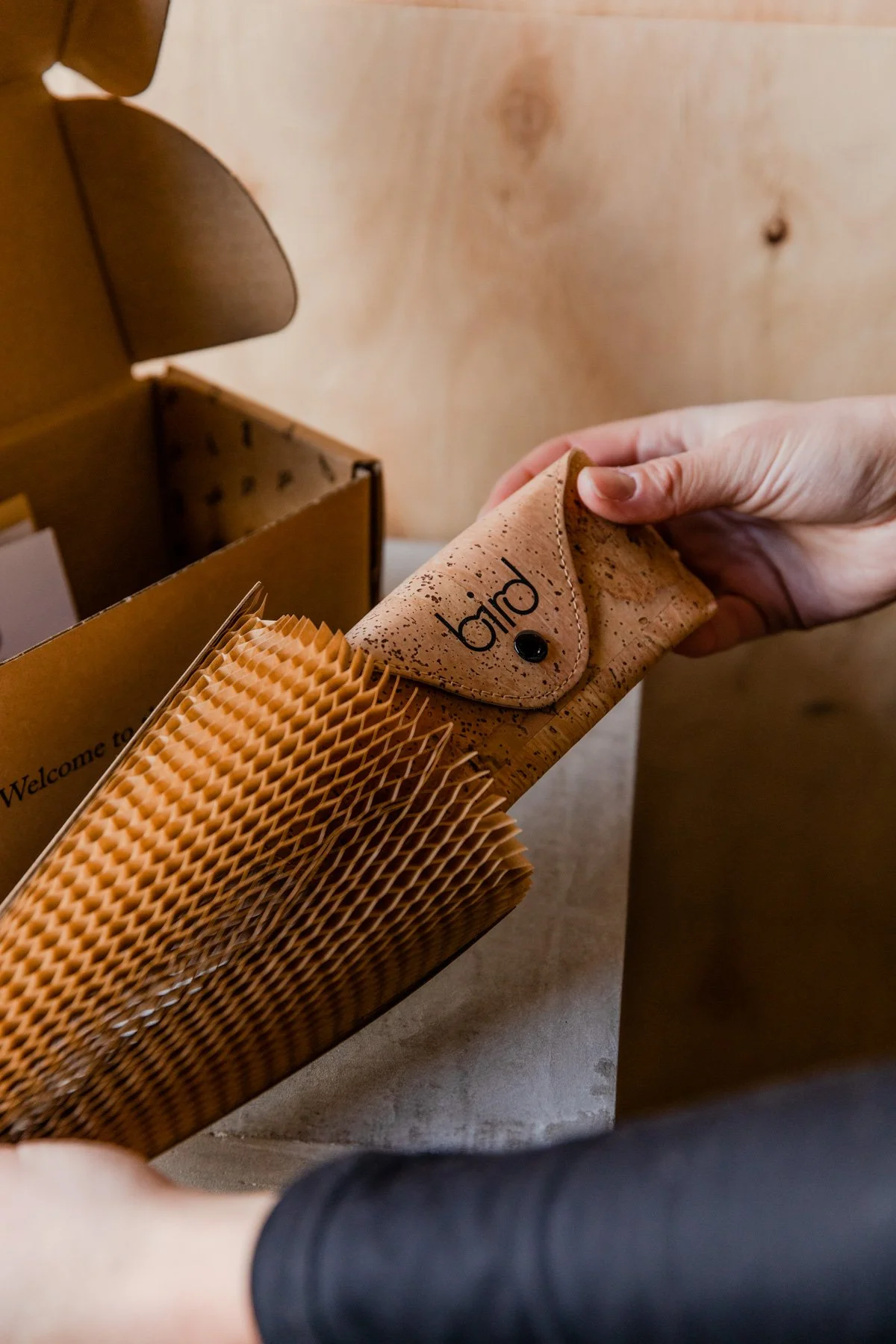 A person holding a cork case with "bird" logo, partially wrapped in honeycomb paper packaging, with a cardboard box nearby.