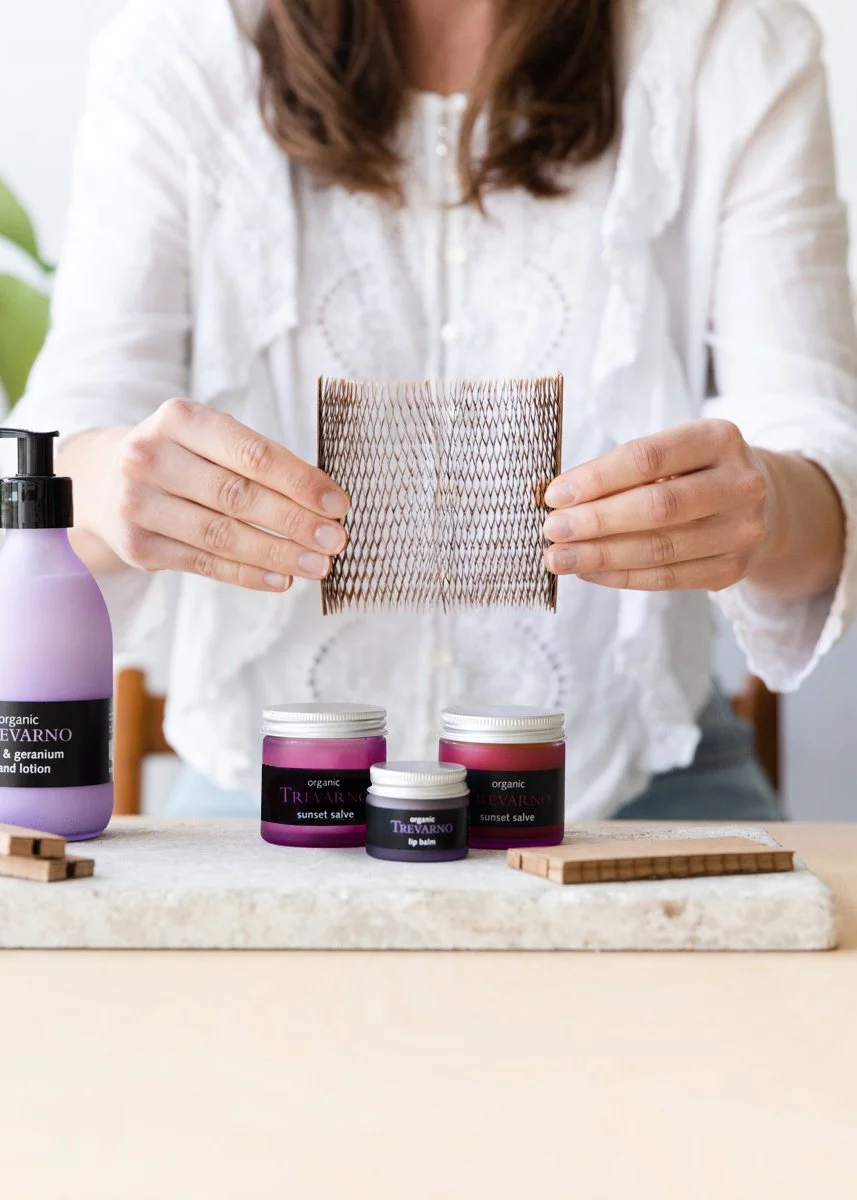 Person with hair visible holding a textured sheet above jars of organic skincare products, including lotion and salves.