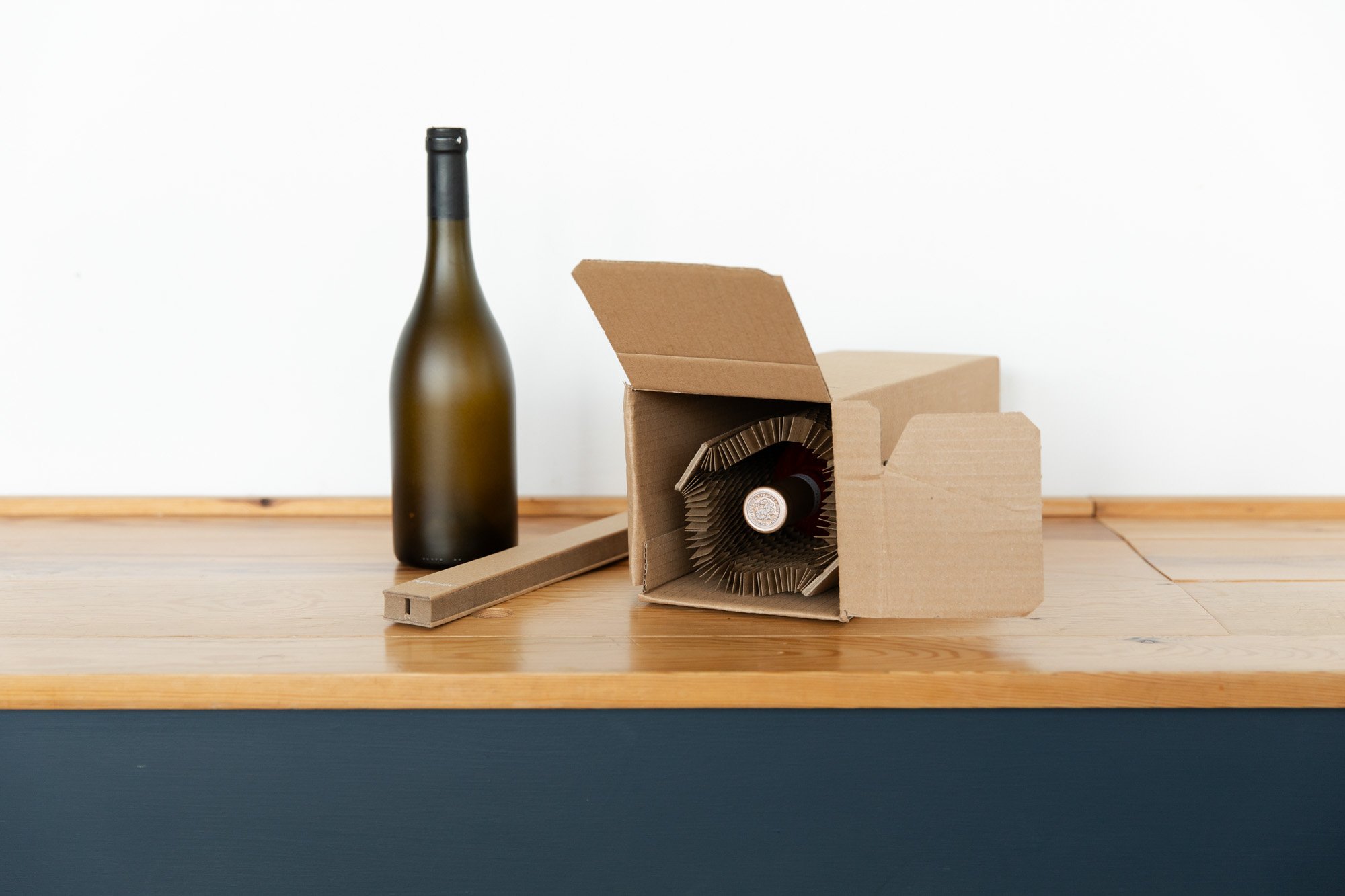 Wine bottle and open cardboard box with protective packaging on wooden surface.