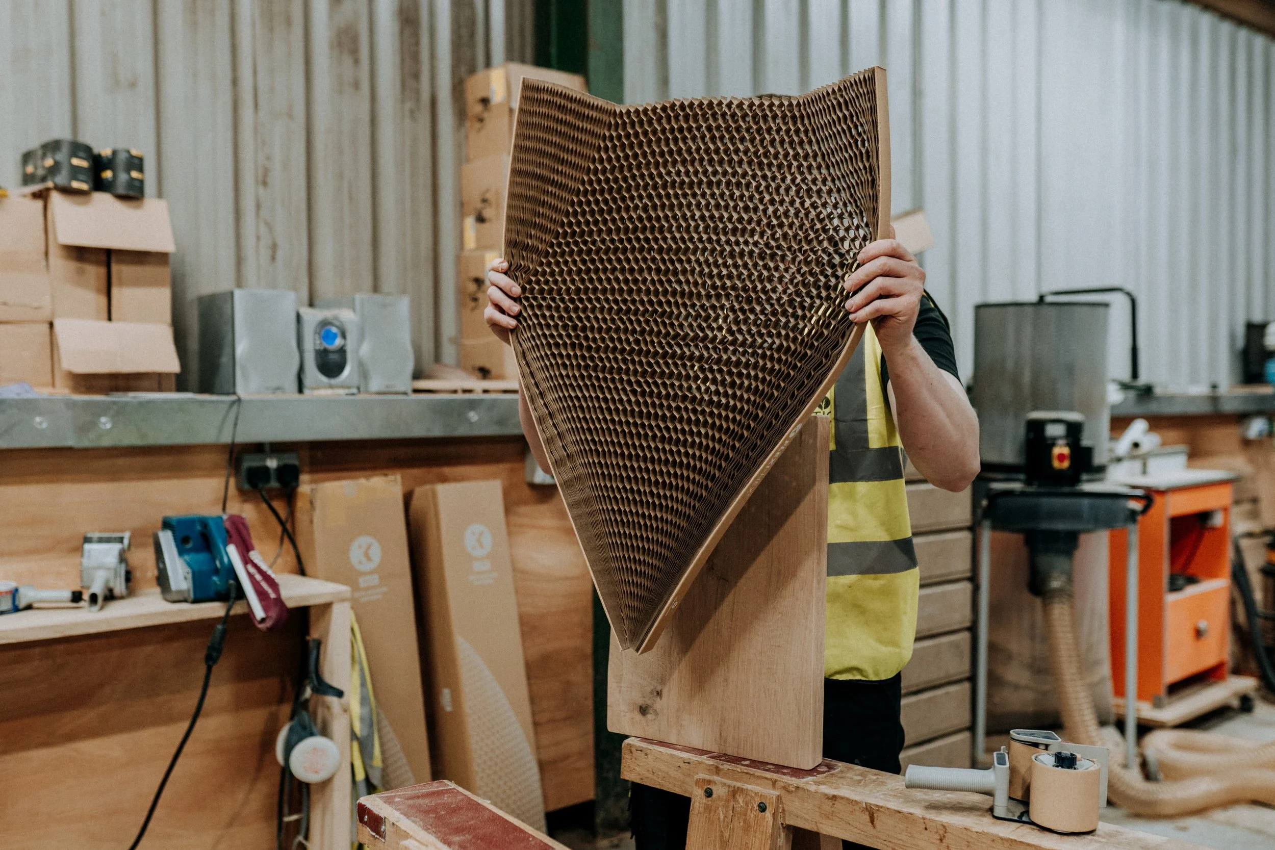 Person holding honeycomb cardboard in workshop, surrounded by boxes and tools.