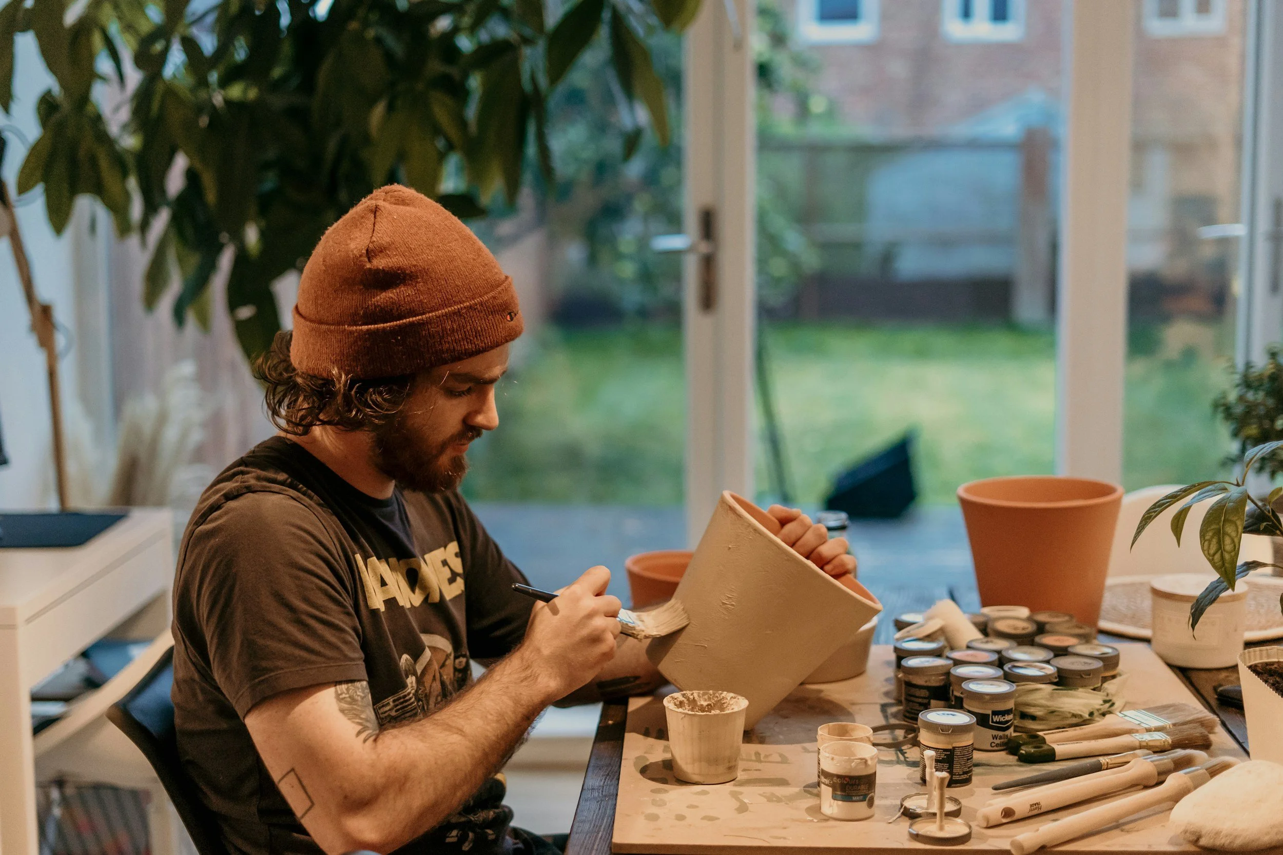Man in beanie works on a collection of pottery.