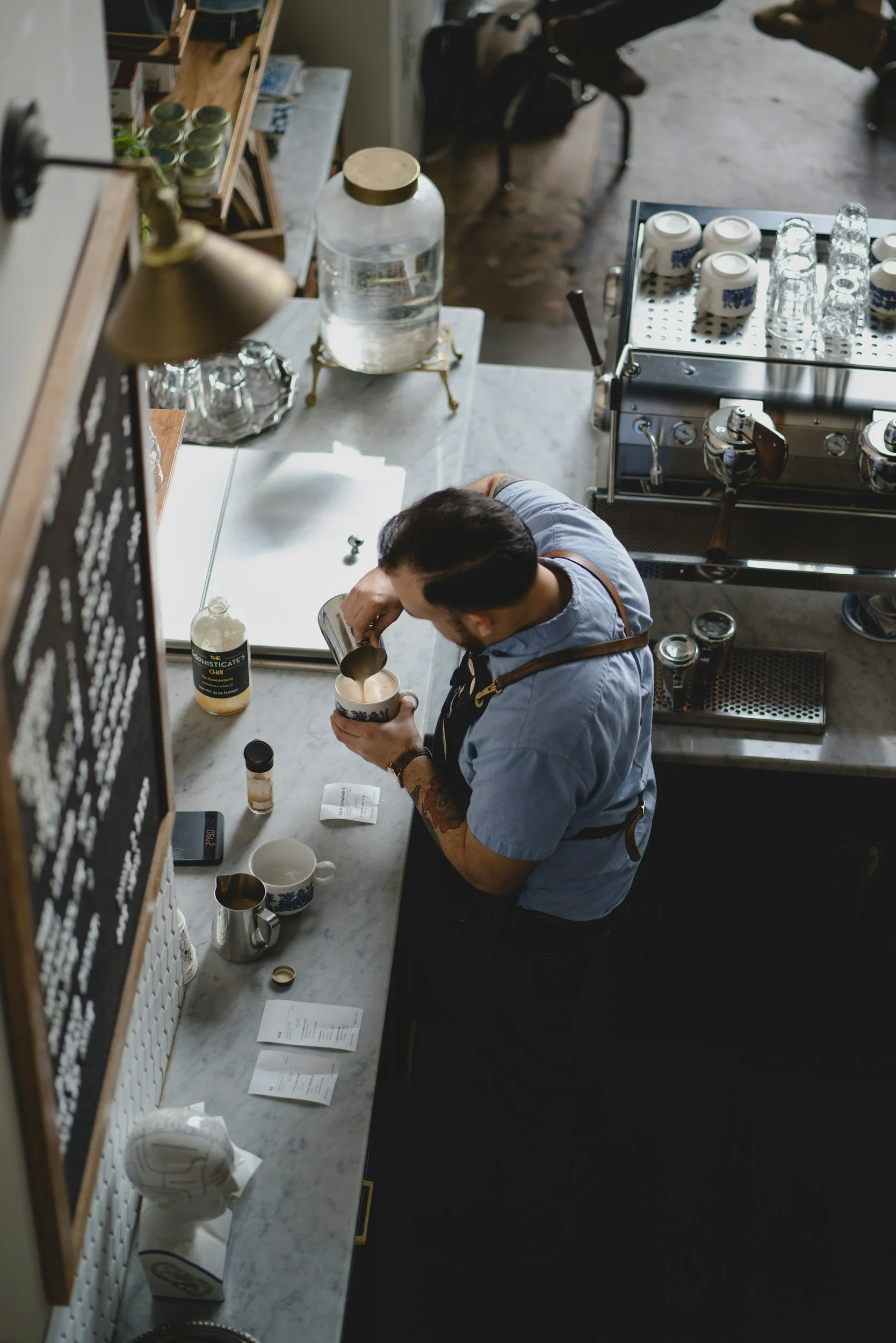 Male barista in blue shirt adding milk to a large cup of coffee