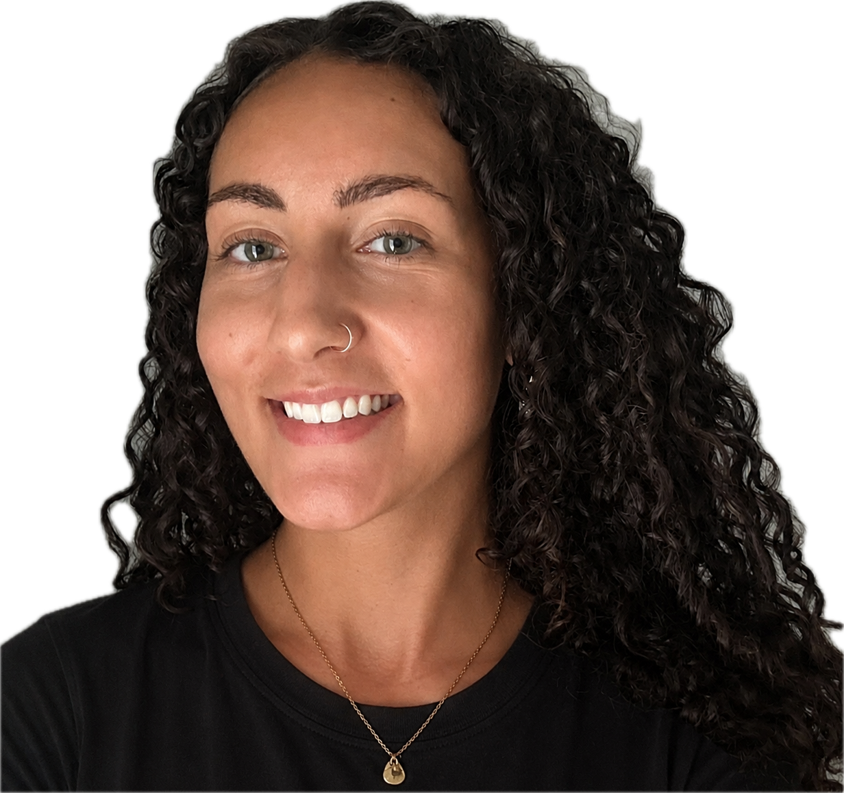 A woman with curly dark hair, light skin, and light-colored eyes, smiling and wearing a white top, a beige and green cardigan, and a gold necklace with a purple gemstone pendant.