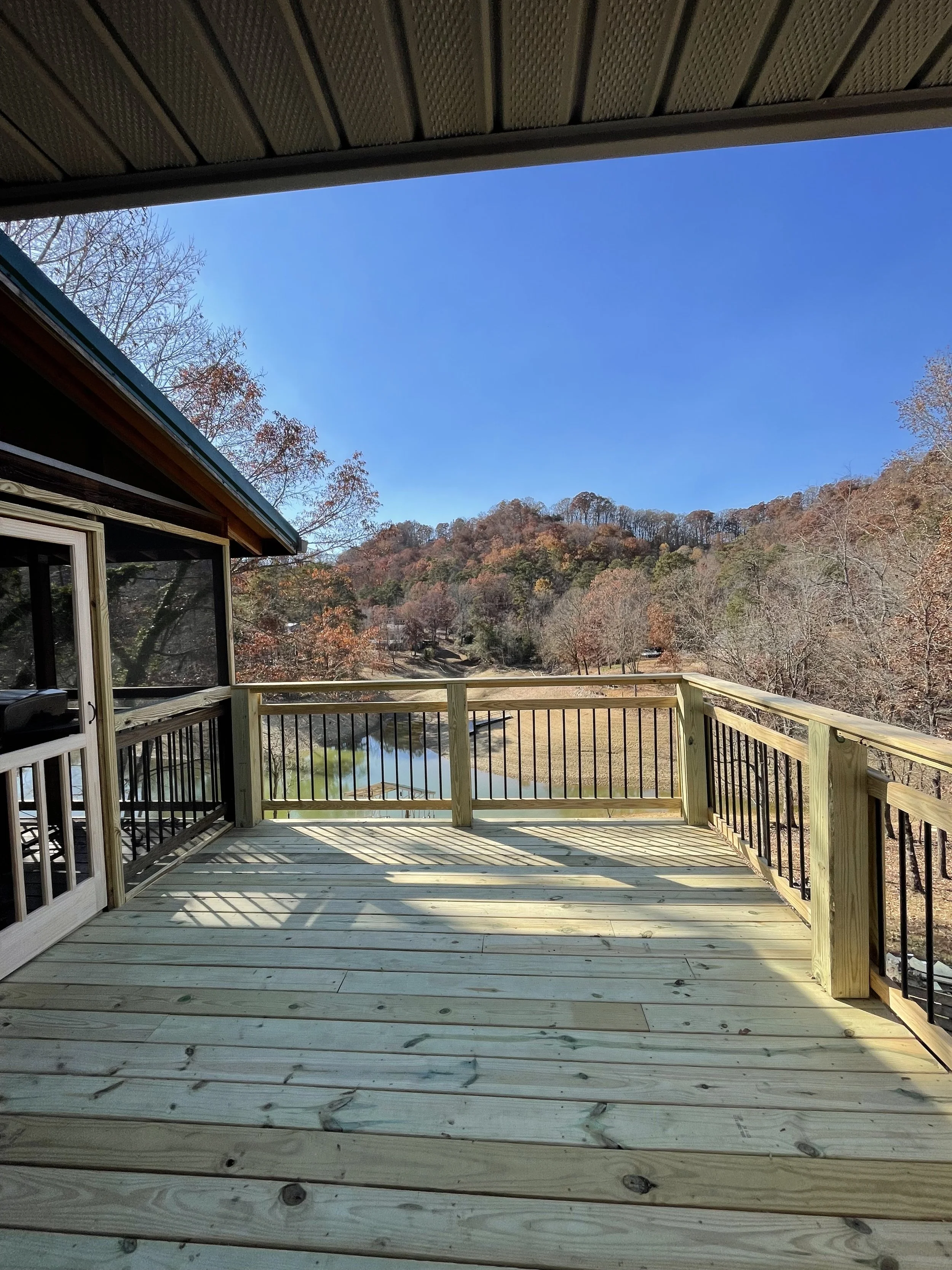 View from a wooden deck overlooking a river, trees with autumn foliage, and a clear blue sky.