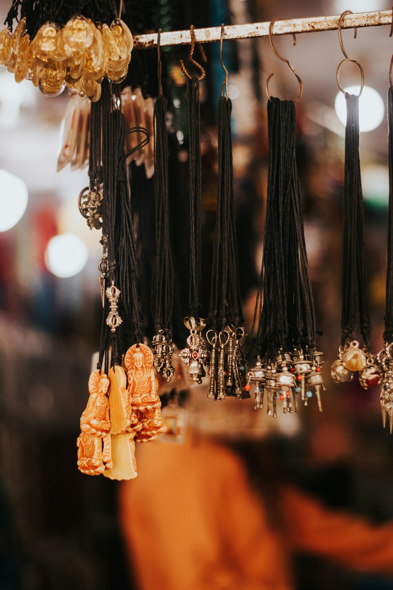 Display of various necklaces with pendants in a market setting, including orange figurine pendants and silver metal charms.