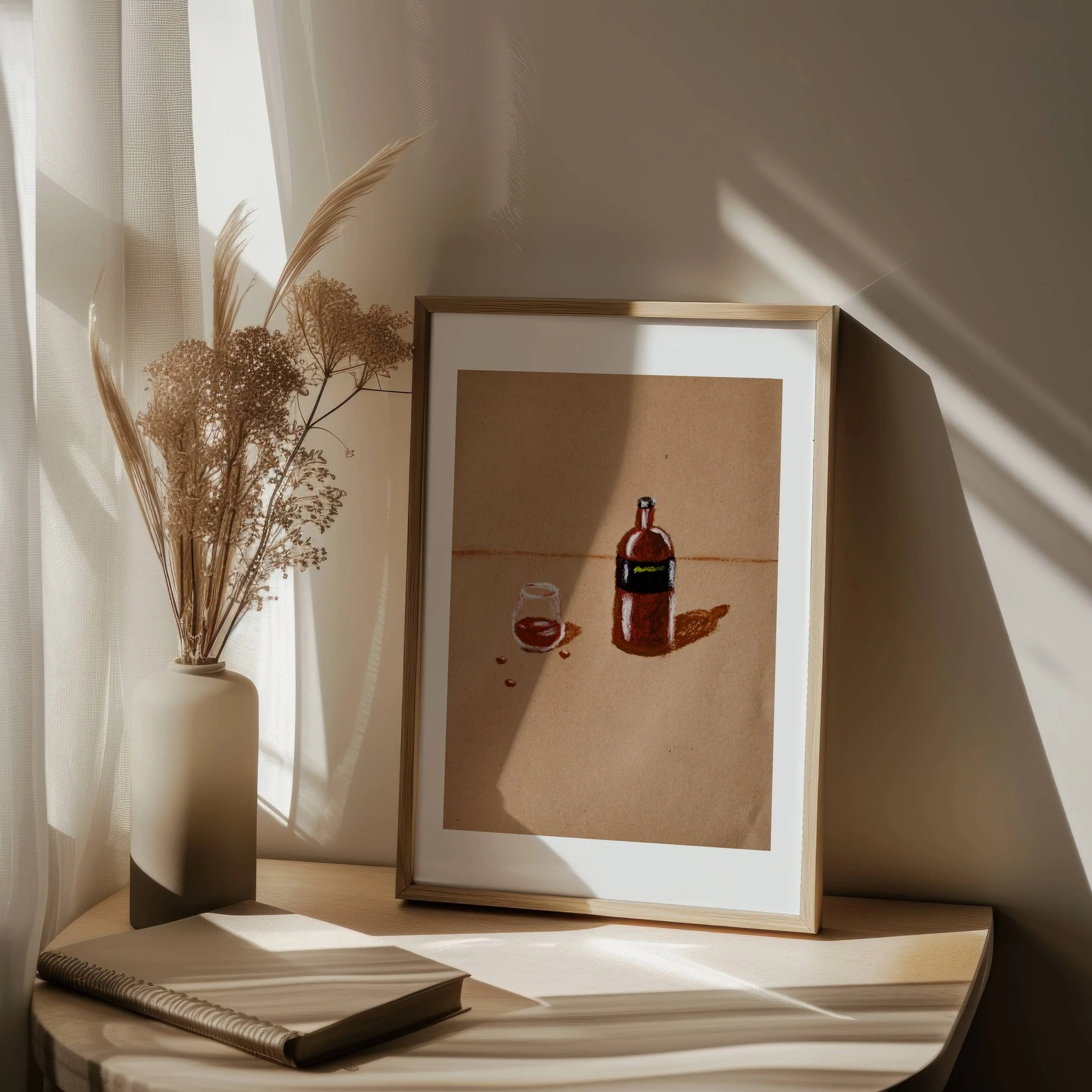 Framed painting of a bottle of red wine, a glass, and a wine cork on a beige background, with dried flowers in a white vase nearby, on a light-colored table.