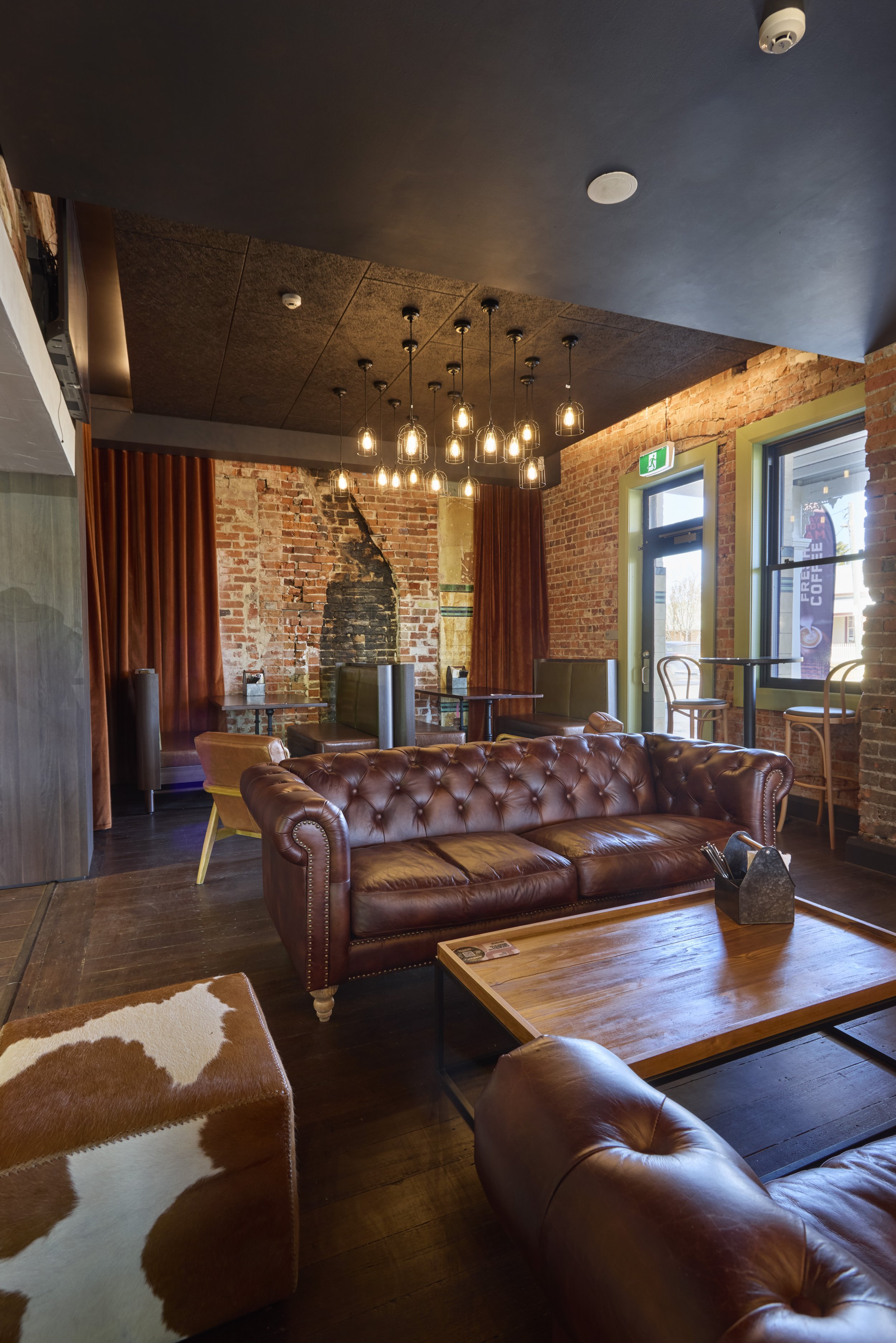 Interior of a cozy café with leather couches, wooden tables, exposed brick walls, mood lighting, and large windows.