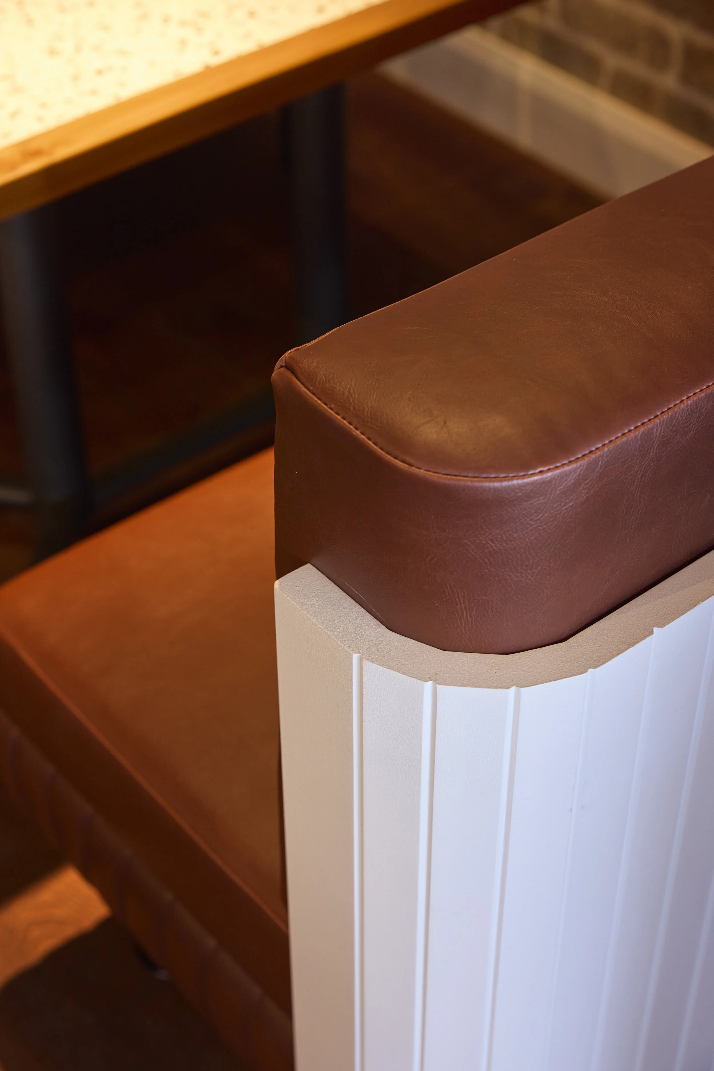 Close-up of a piece of furniture with a curved, brown leather surface and white wooden panels decorated with vertical grooves.