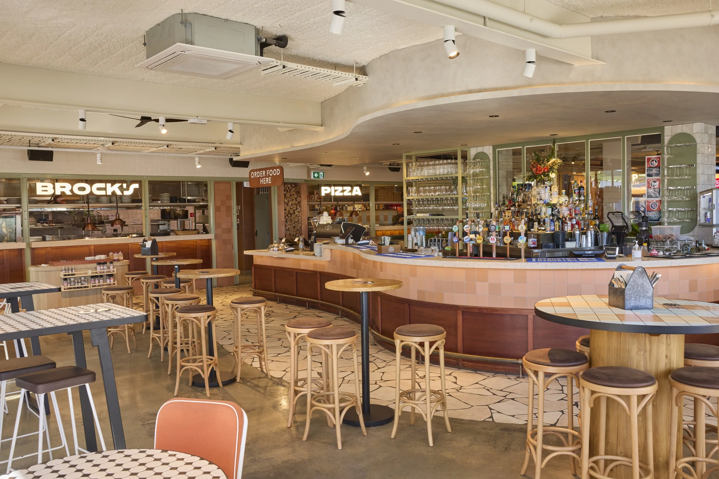 Interior of a restaurant with bar area and tables, signs for food ordering and pizza, and various bottles and glasses on shelves behind the bar.