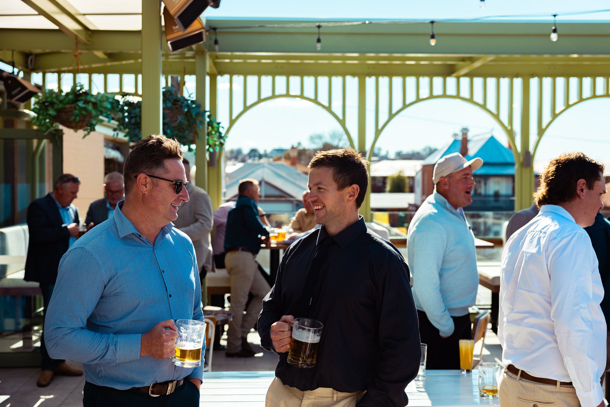 People socializing on a rooftop patio, holding drinks during daytime.