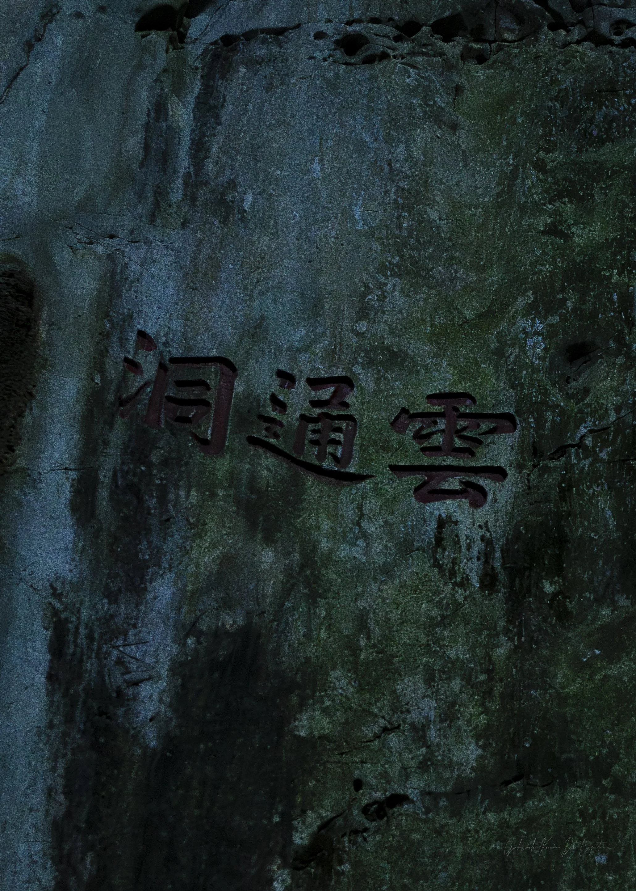 A dark, textured rock or stone wall with some Chinese or Asian characters painted in red and black ink on its surface.