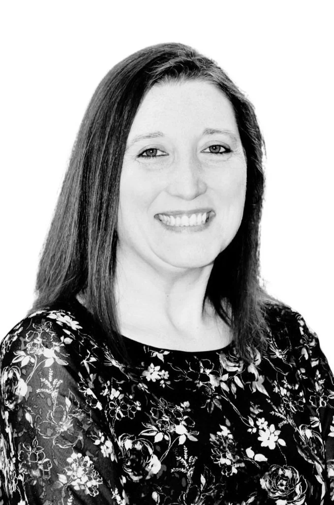 Black and white portrait of a smiling woman with long hair wearing a floral top.