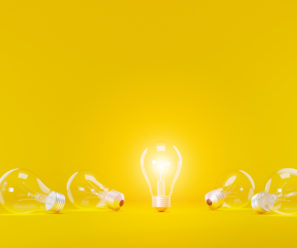 Five light bulbs on a yellow background; four are unlit and lying down, while one is lit and standing upright in the center.