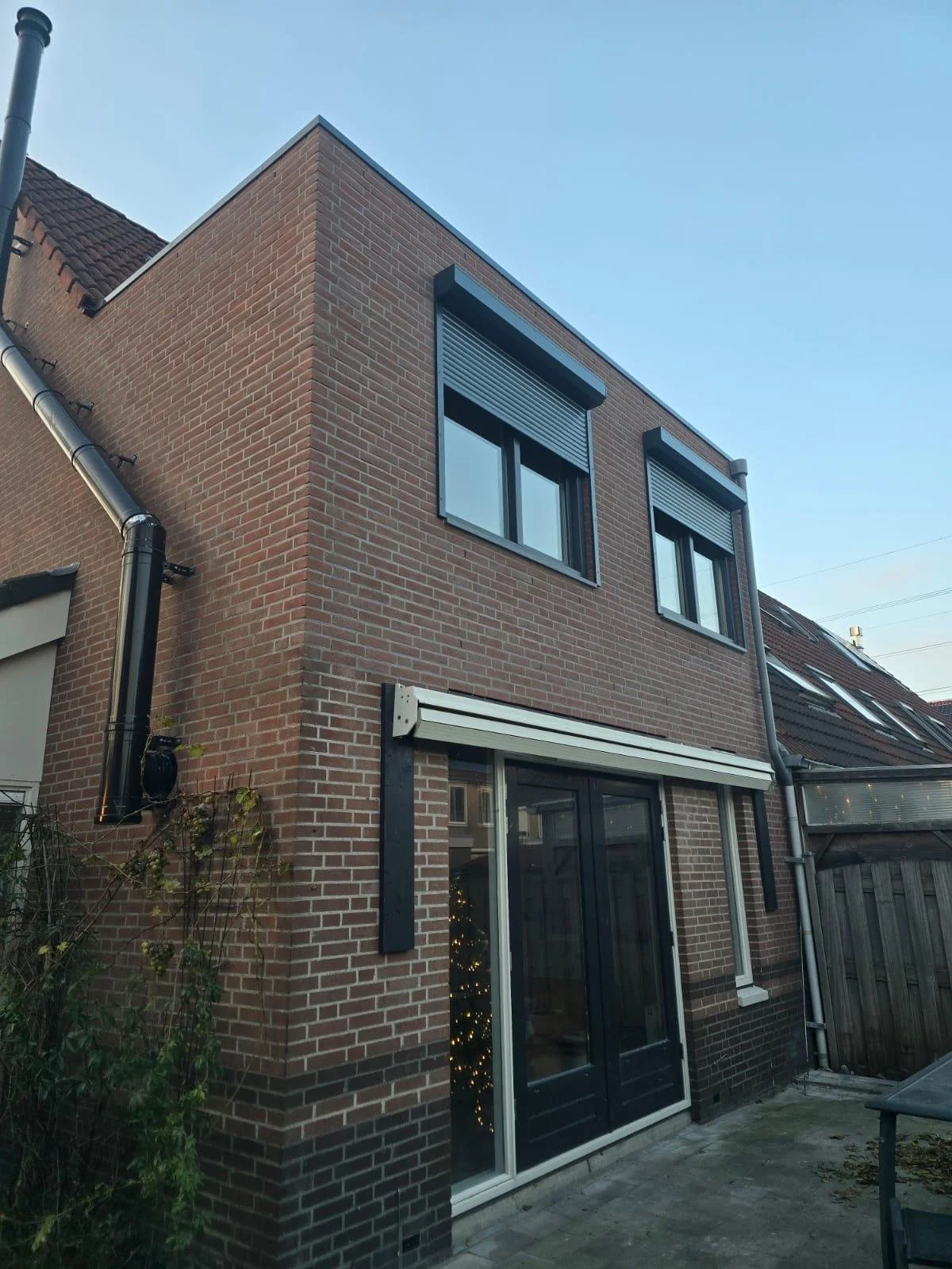 Een modern bakstenen huis met grote ramen en een patio, tijdens de dag met een duidelijke blauwe lucht.