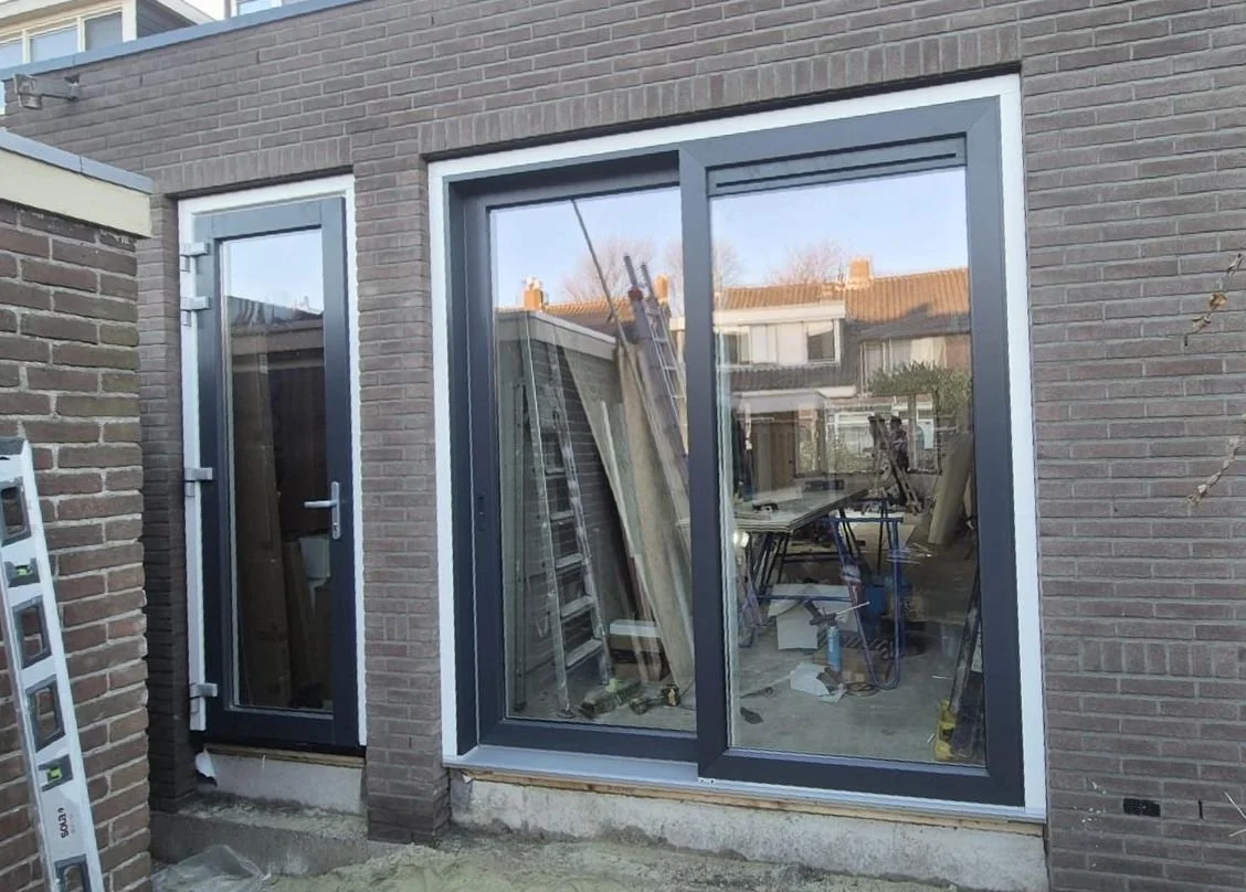 Nieuwbouwproject met grote glazen schuifdeuren en een deur, bouwmaterialen en gereedschap binnen en buiten de woning.