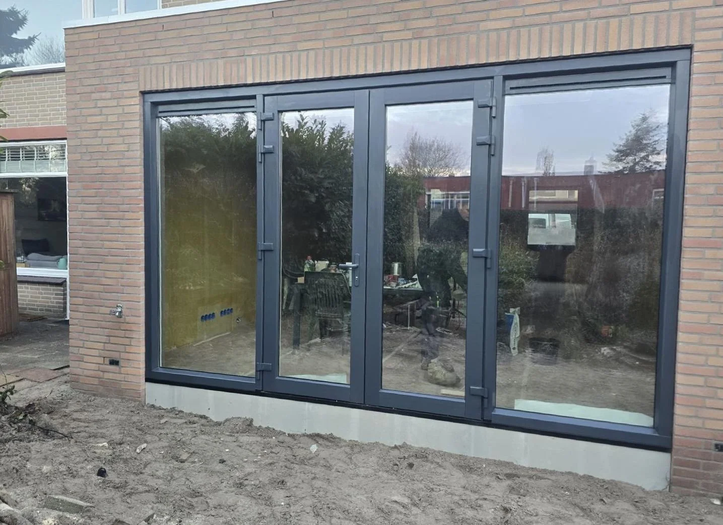 Nieuwe glazen tuindeur geïnstalleerd in een bakstenen muur, met nog steeds een bouwplaats voor de deur.