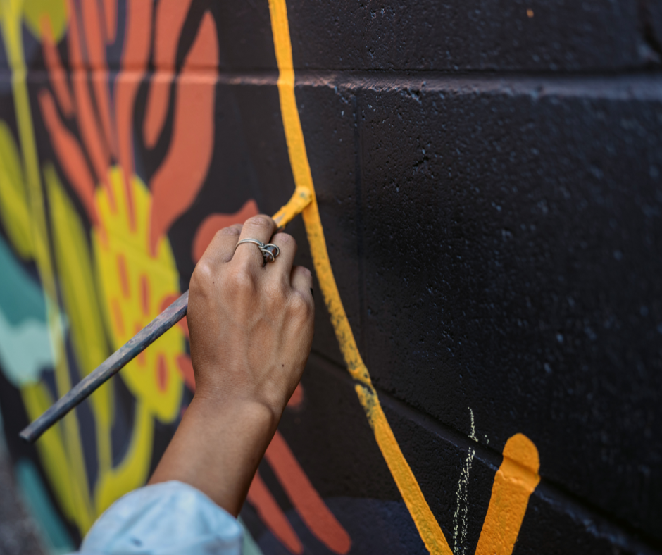 Close-up of a mural artist outlining a colourful design on a brick wall, showcasing precision and vibrant detail in a commercial mural project.