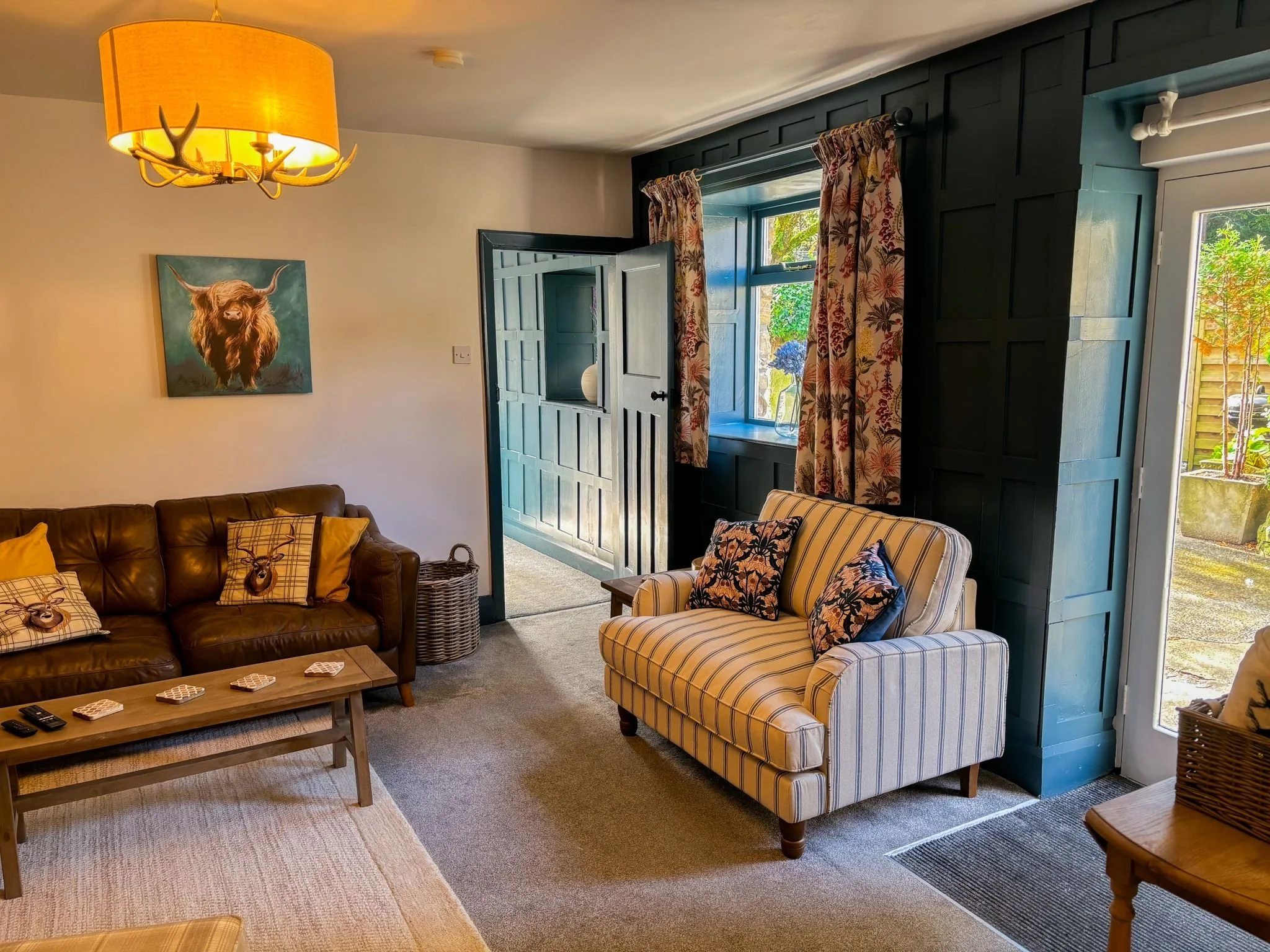 Living room decorated by Haslam Decor, featuring a brown leather sofa, striped armchair, Highland cow artwork, and floral curtains in a warm, inviting setting.